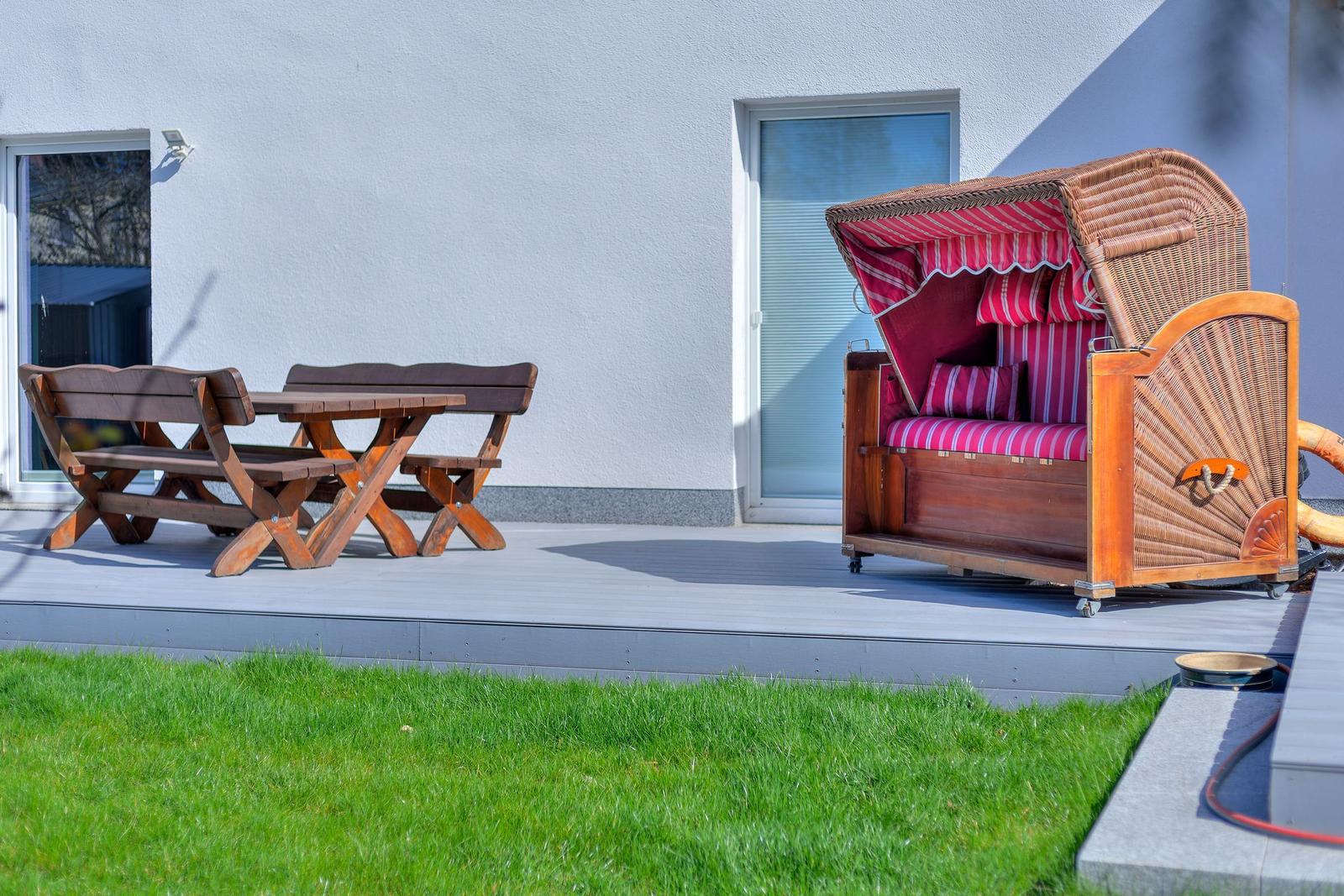 Terrasse mit Holztisch, Bänken und Strandkorb mit rotem Streifenstoff.