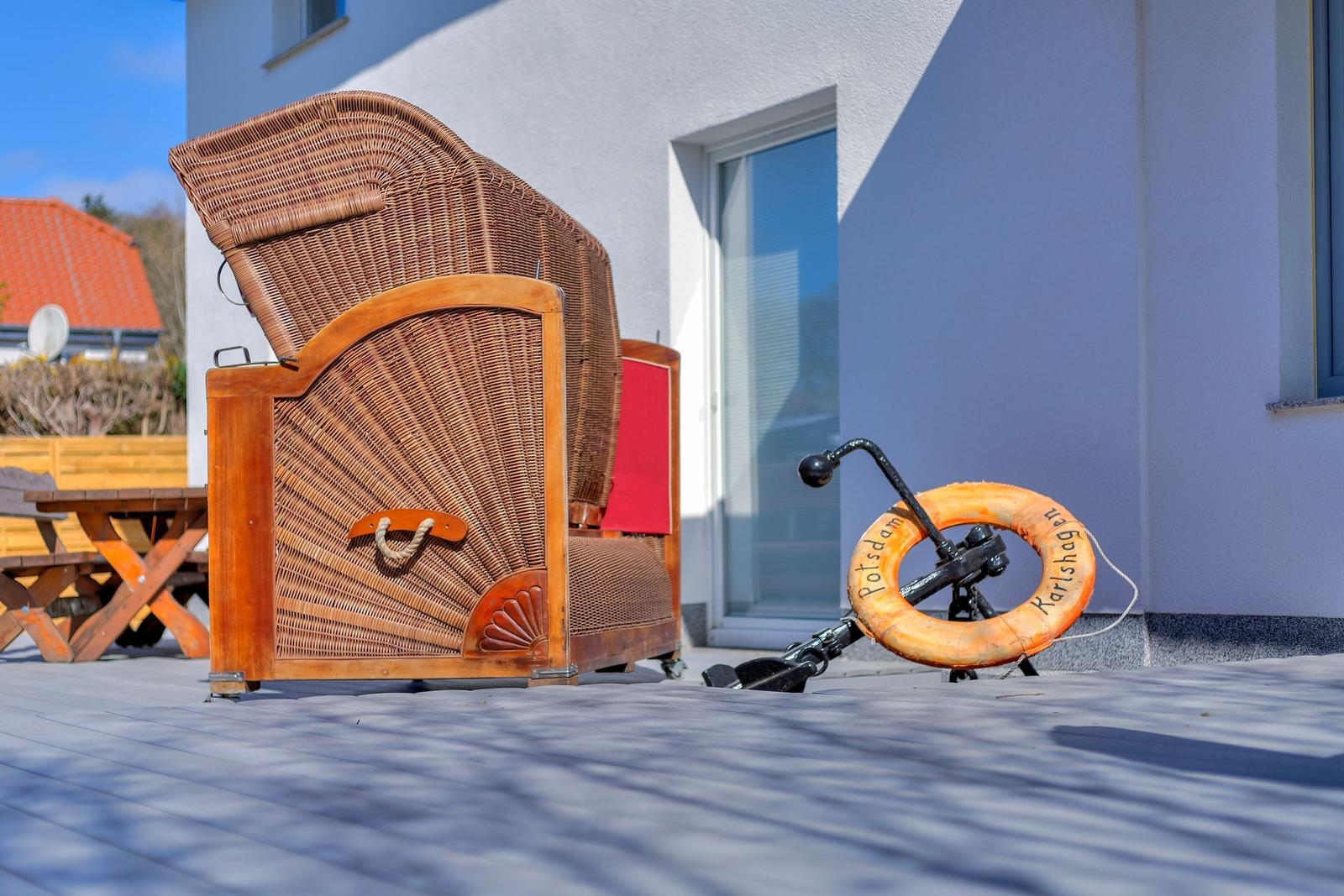 Außenterrasse mit Rattan-Sofa und Rettungsring. Hintergrund: weißes Haus mit Fenster.