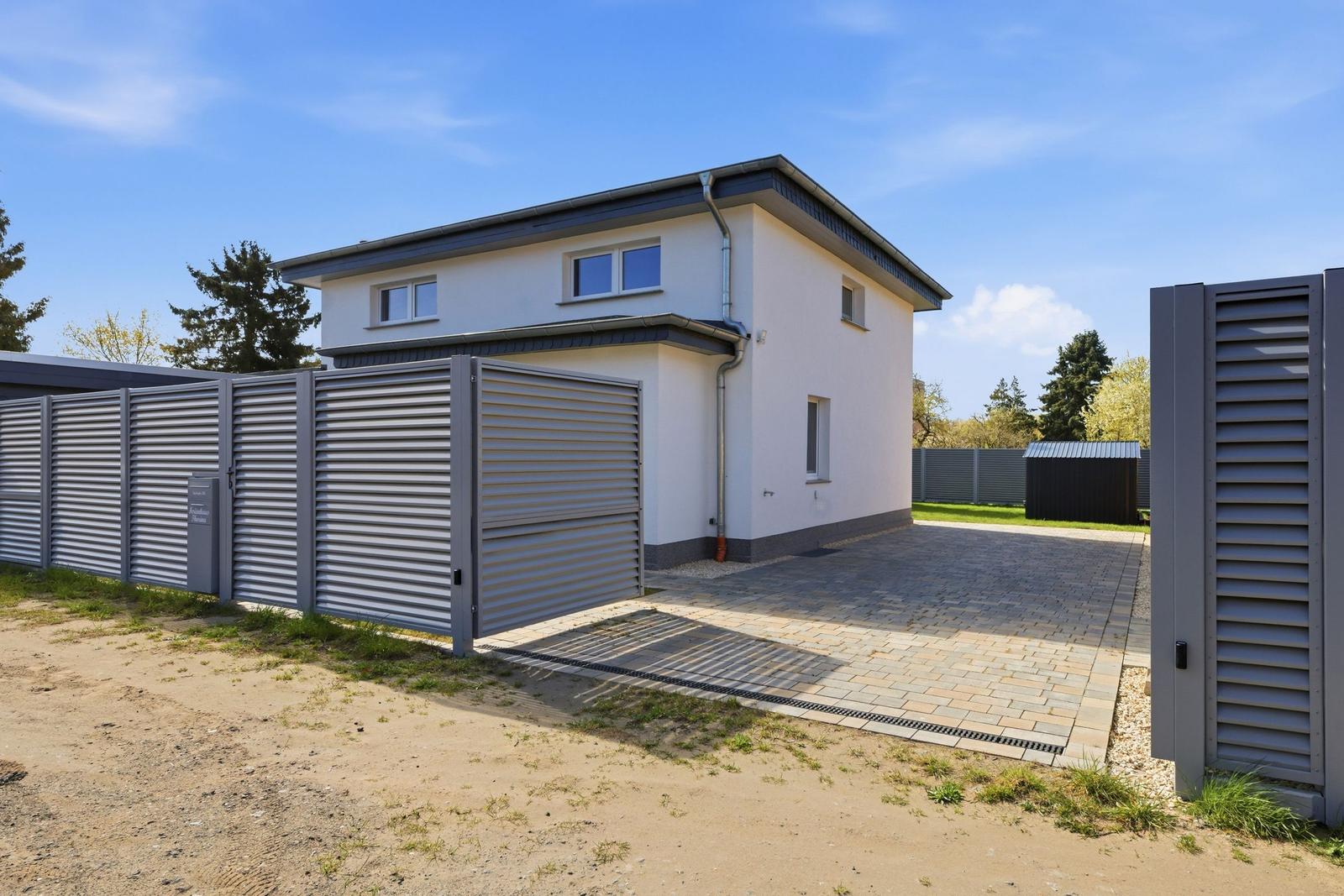 Moderne Villa mit Garagenbereich und gepflastertem Hof. Umzäunt mit metallischem Zaun.