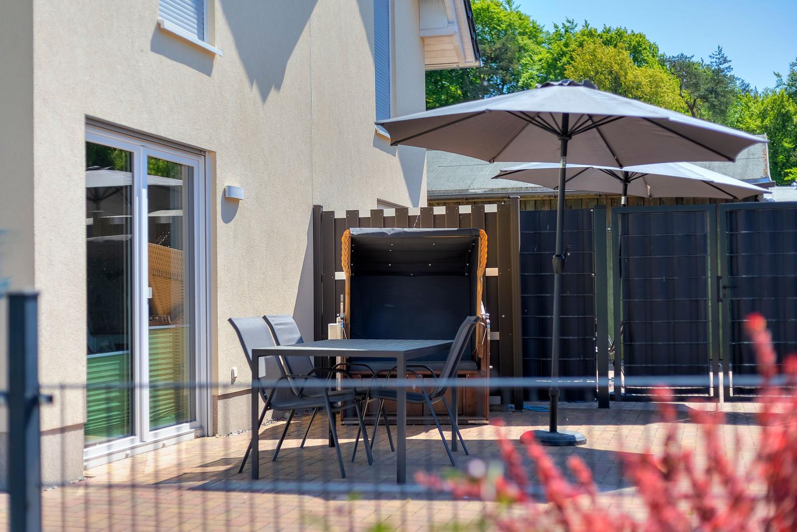 Terrace with table, chairs, and umbrellas. Backyard with fence and trees.