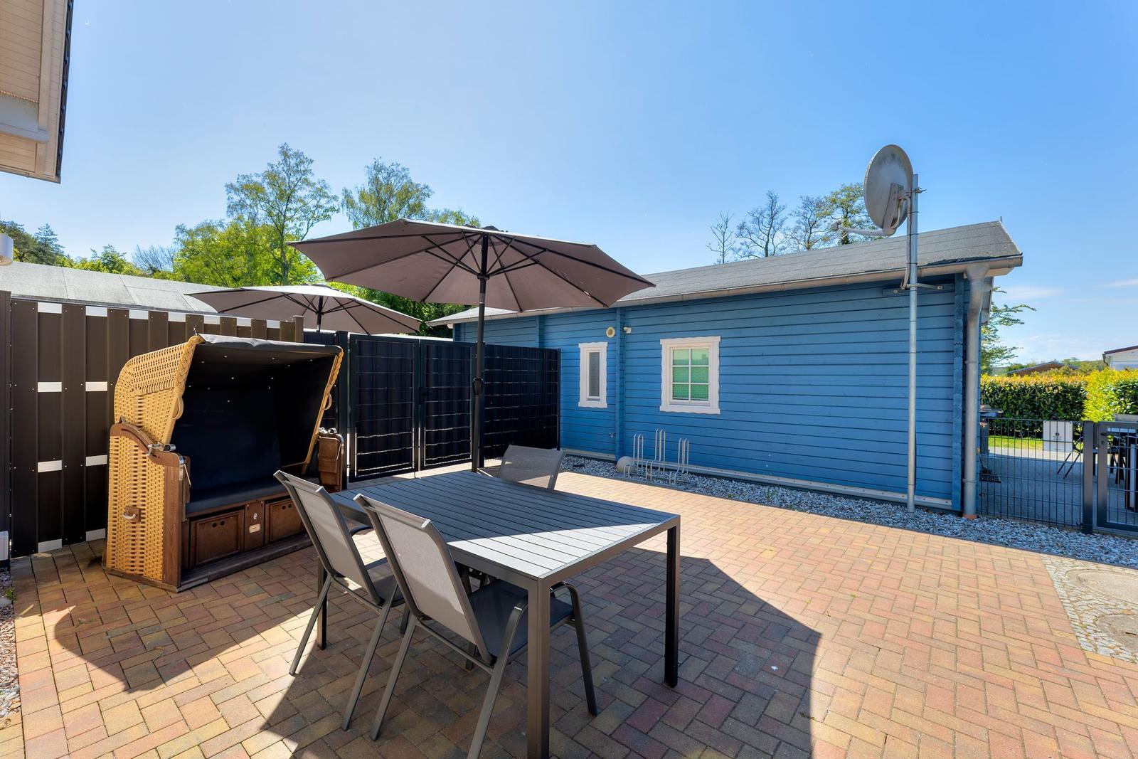 Terrace with table, chairs, and umbrellas next to blue house.