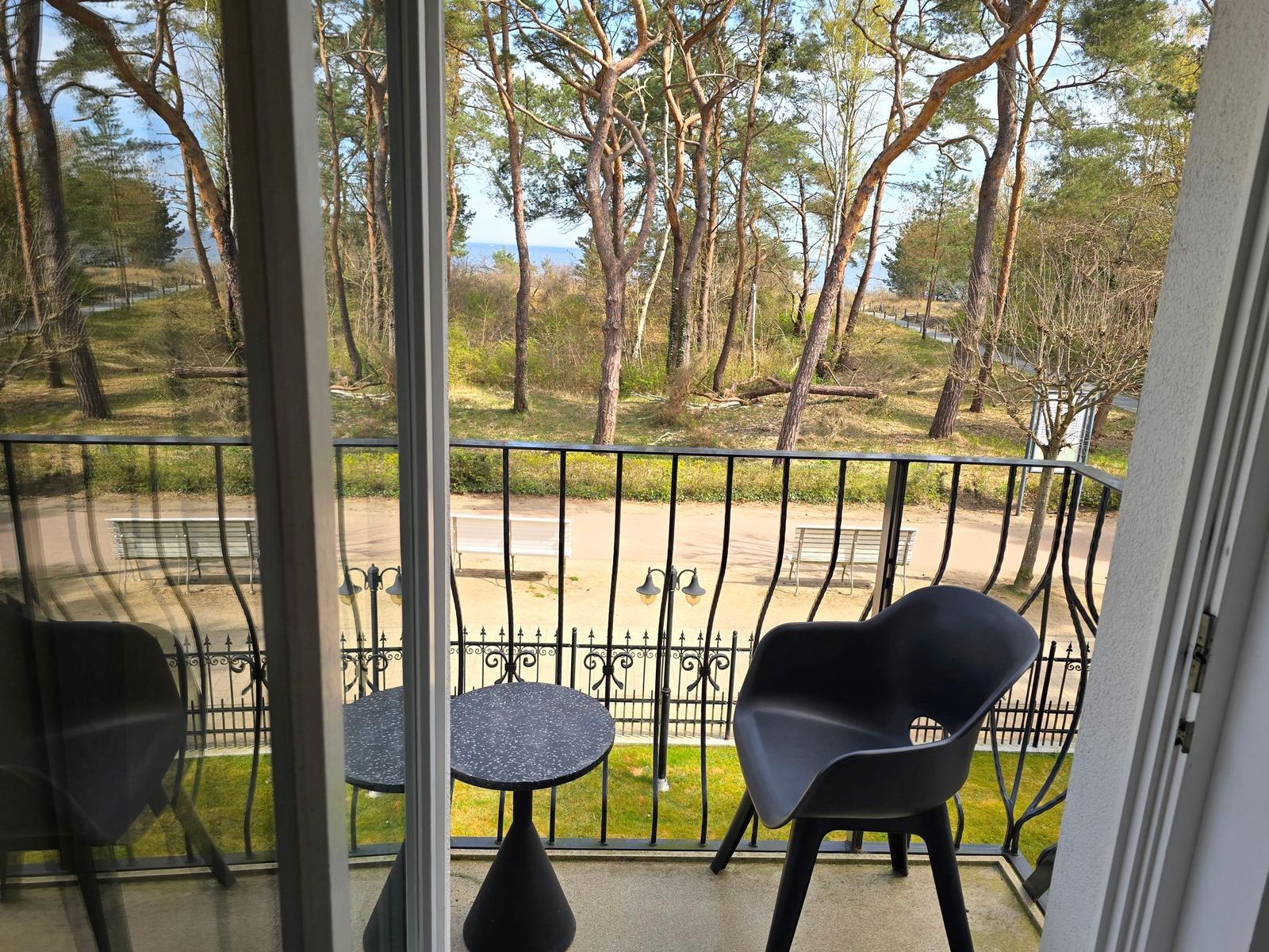 Balkon mit Tisch und Stuhl, Blick auf Wald und Strand.