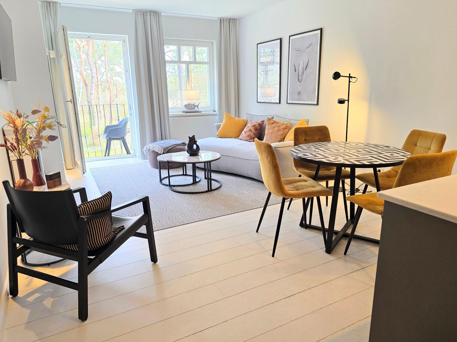 Wohn- und Essbereich mit Sofa, Tisch und Stühlen. Durchgang zur Terrasse mit Blick auf Wald.