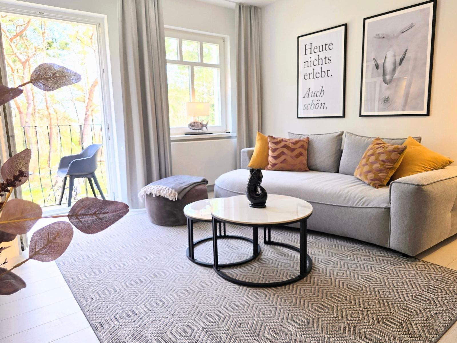 Wohnzimmer mit Sofa, Tisch und Blick auf Balkon mit Garten.