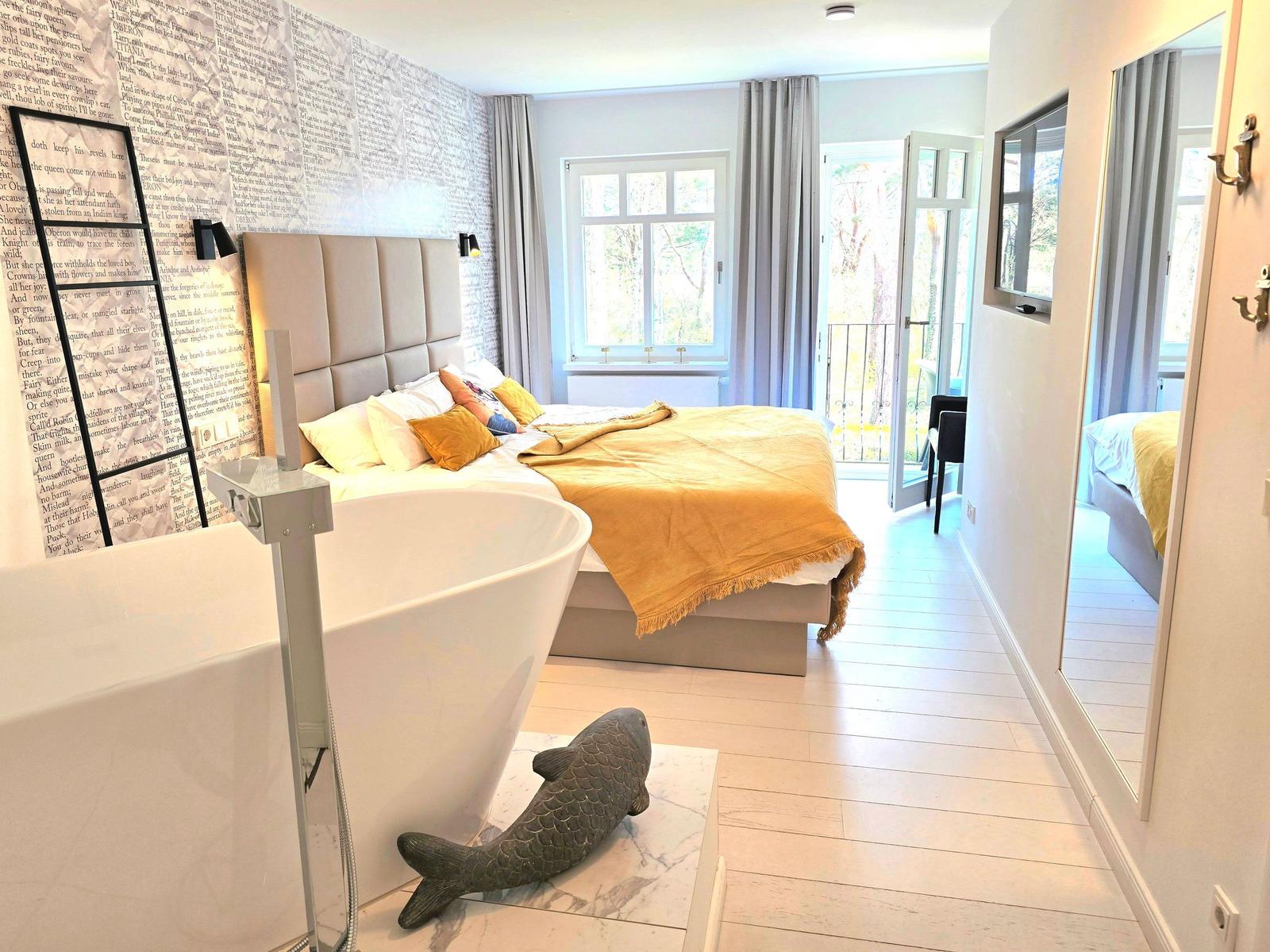 Schlafzimmer mit Badewanne, Bett und Balkon. Wand mit Text und Fischfigur.