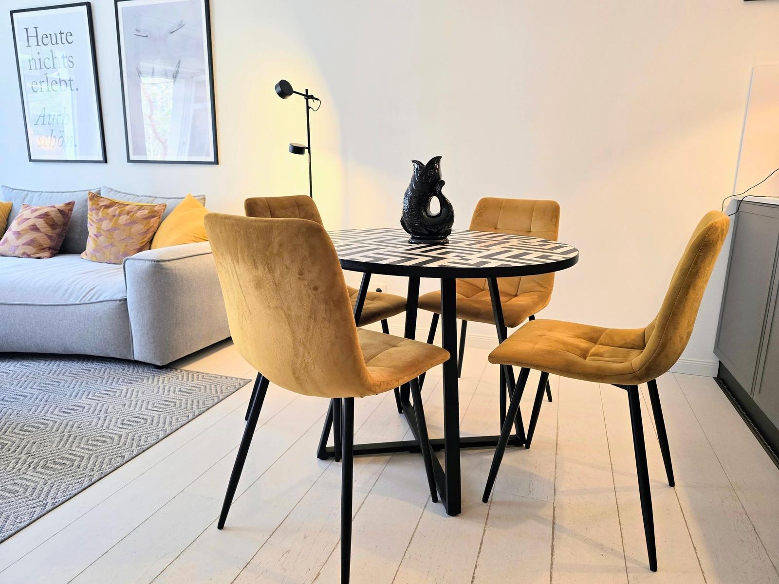 Runder Tisch mit vier Stühlen und Sofa im Hintergrund.