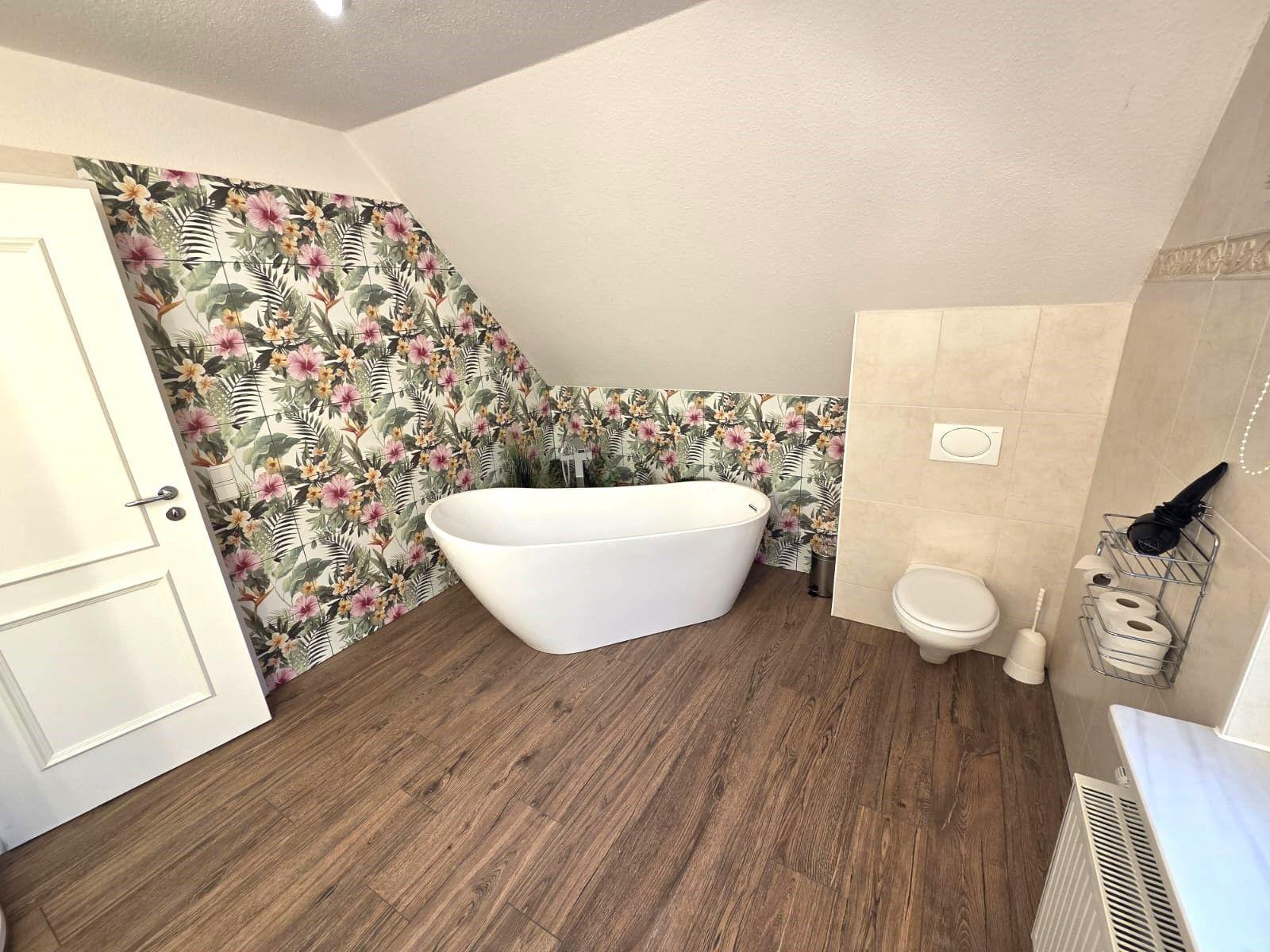 Badezimmer mit freistehender Badewanne, floraler Wand und Holzfußboden.