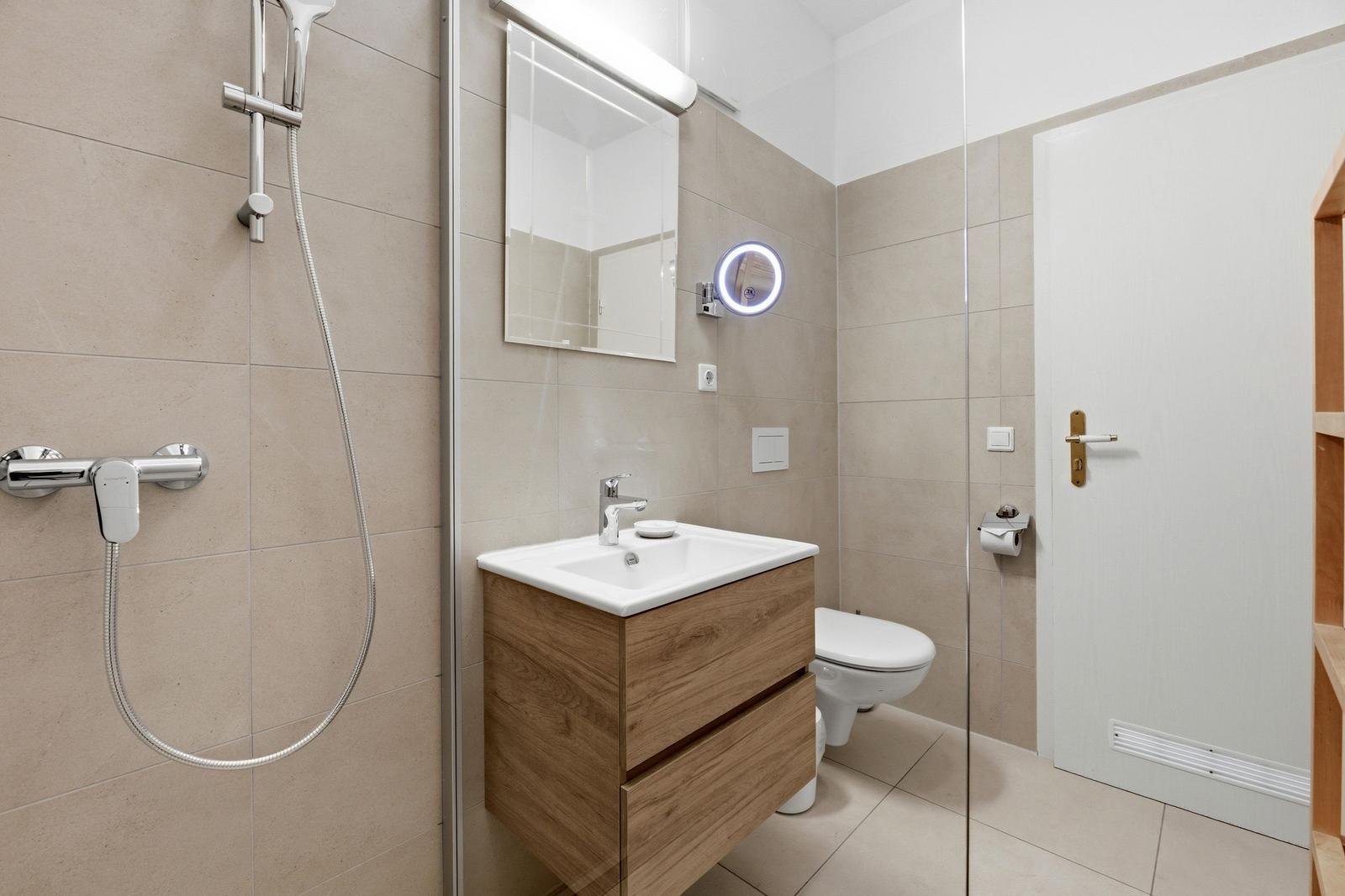 Bathroom with shower, sink and toilet. Wooden vanity and illuminated mirror.