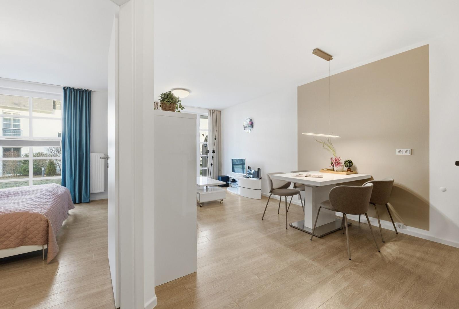 Wohnung mit Essbereich, Schlafzimmer und Wohnzimmer. Holzboden, weiße Möbel und moderne Beleuchtung.
