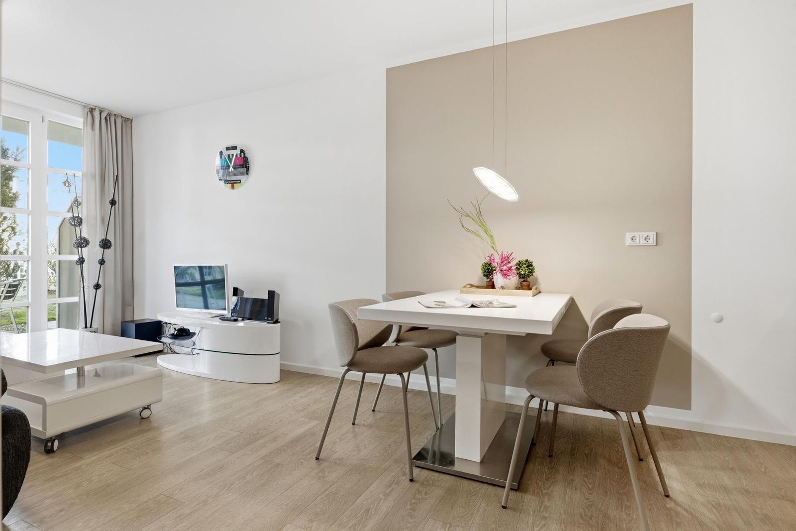 Essbereich mit weißem Tisch und Stühlen, Wohnbereich mit TV und Fenster.