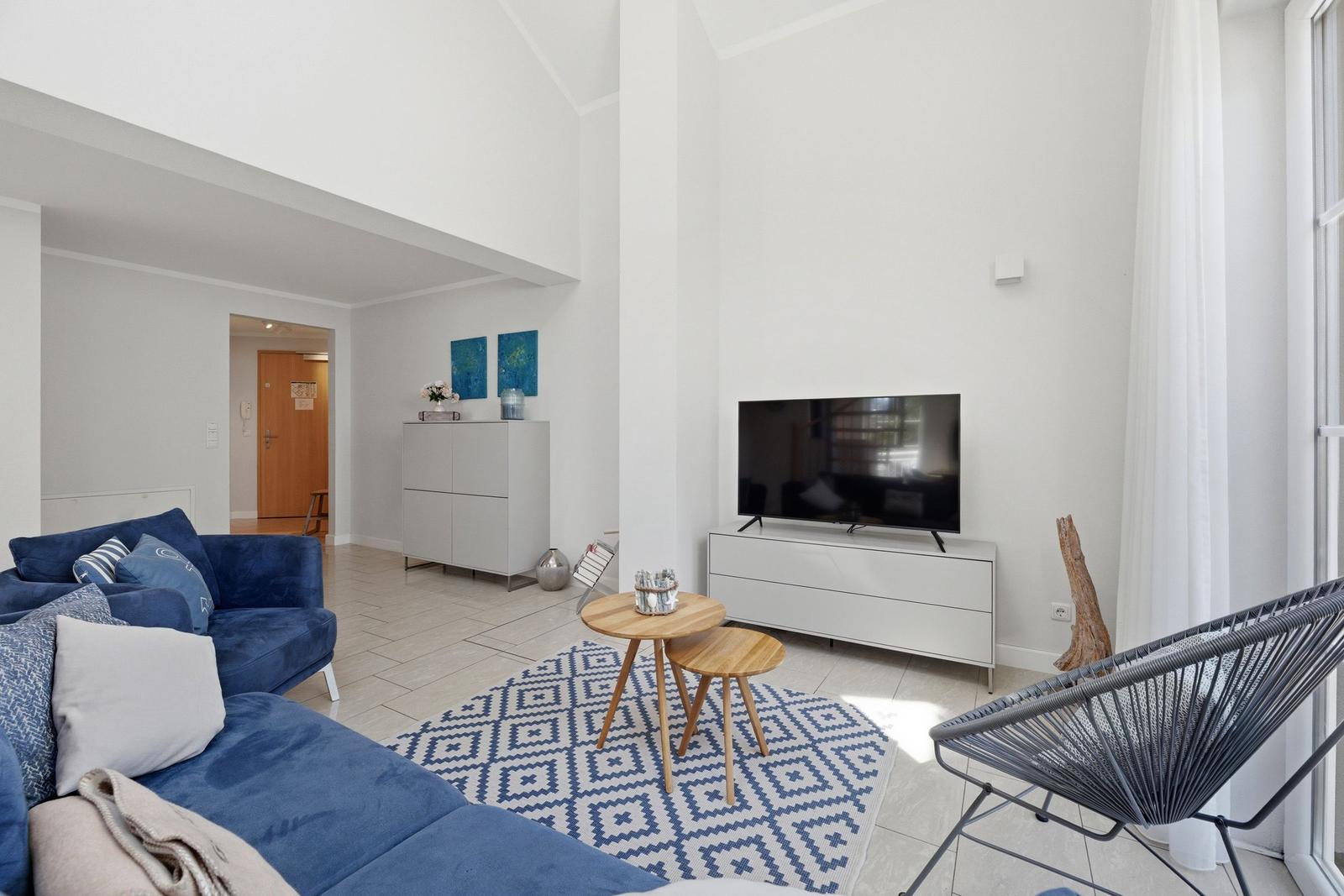 Wohnzimmer mit blauem Sofa, TV und Holztisch auf gemustertem Teppich.