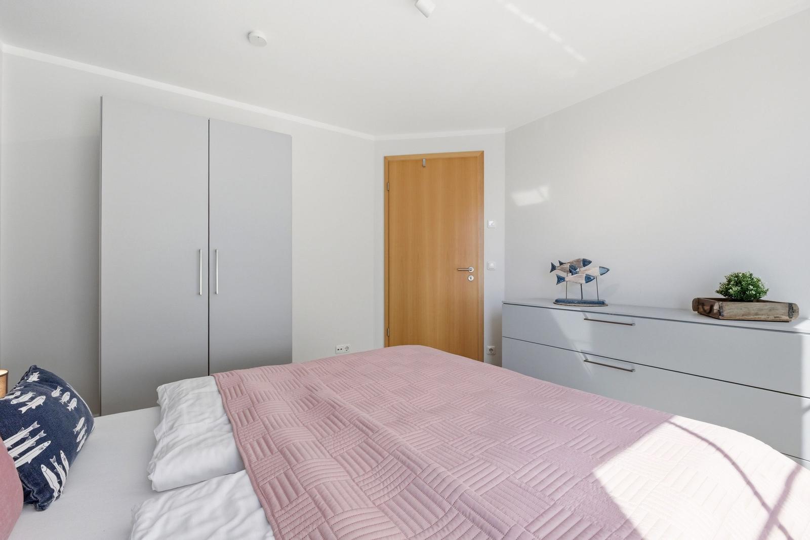 Schlafzimmer mit Bett, Kleiderschrank und Schrank. Dekoration mit Fischfigur und Pflanze.