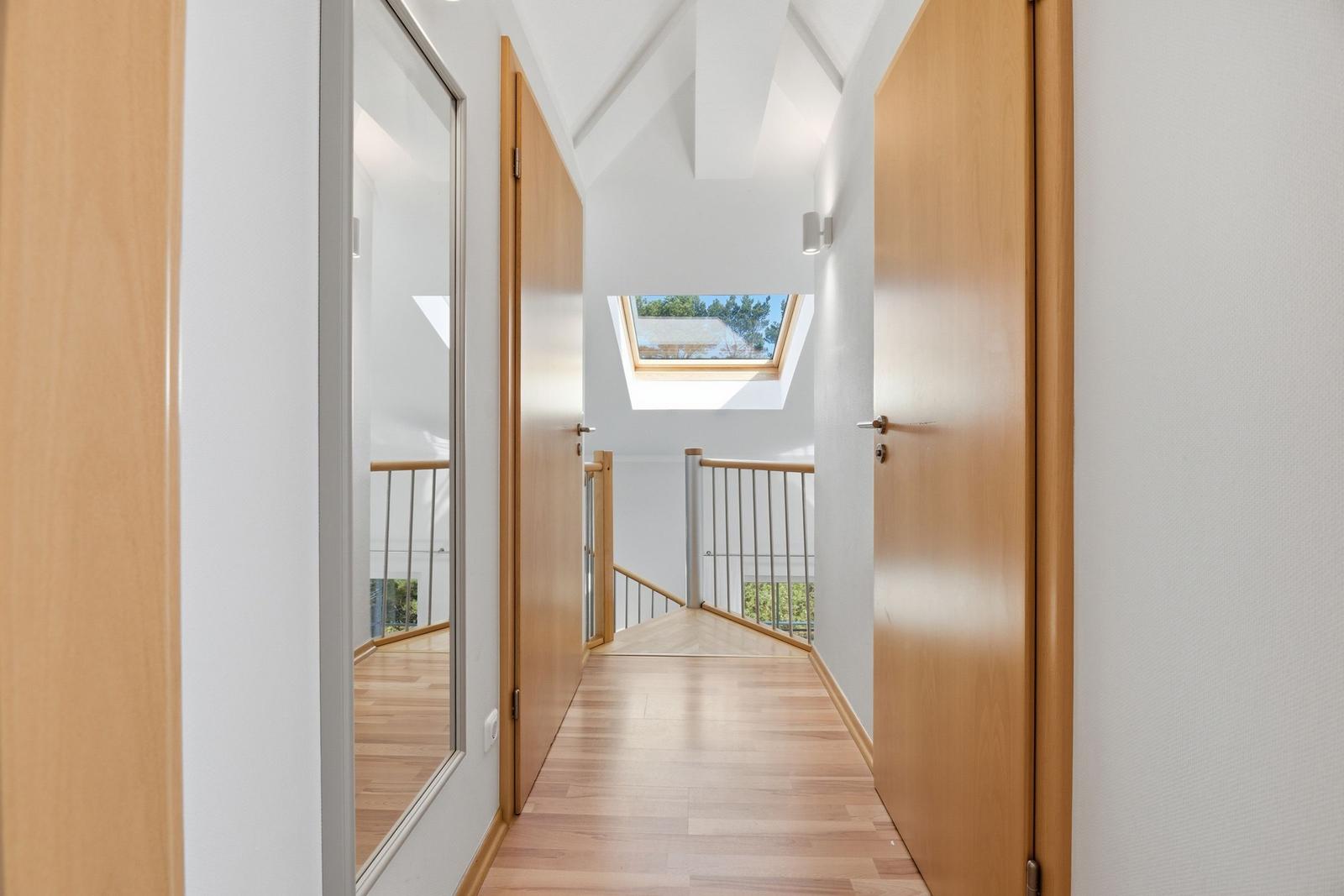 Flur mit Holzboden, Türen und Dachfenster. Geländer und Spiegel sichtbar.