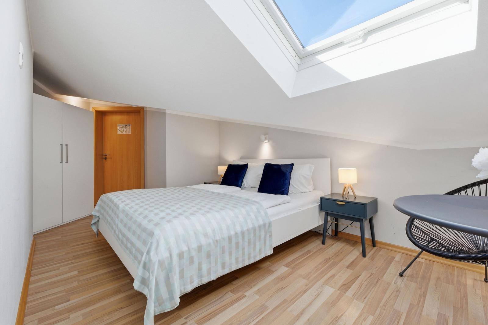 Schlafzimmer mit Dachfenster, Bett, Nachttisch und Schrank.