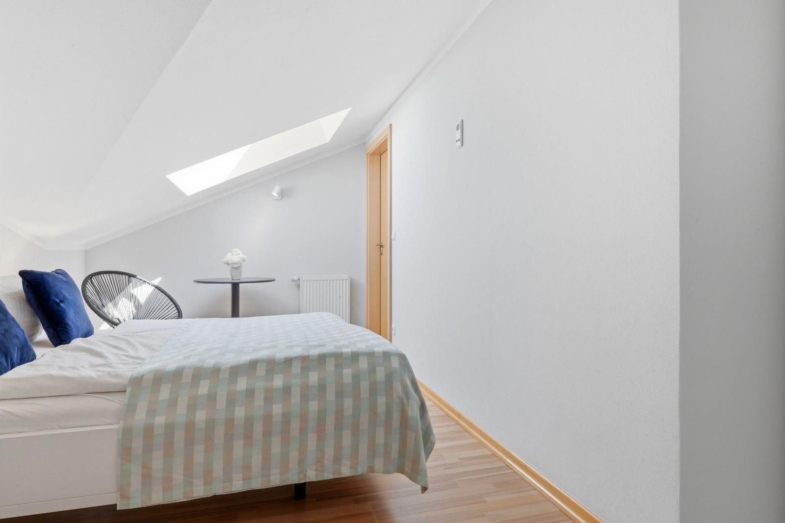 Schlafzimmer mit Dachschräge, Bett, Sessel und Dachfenster.