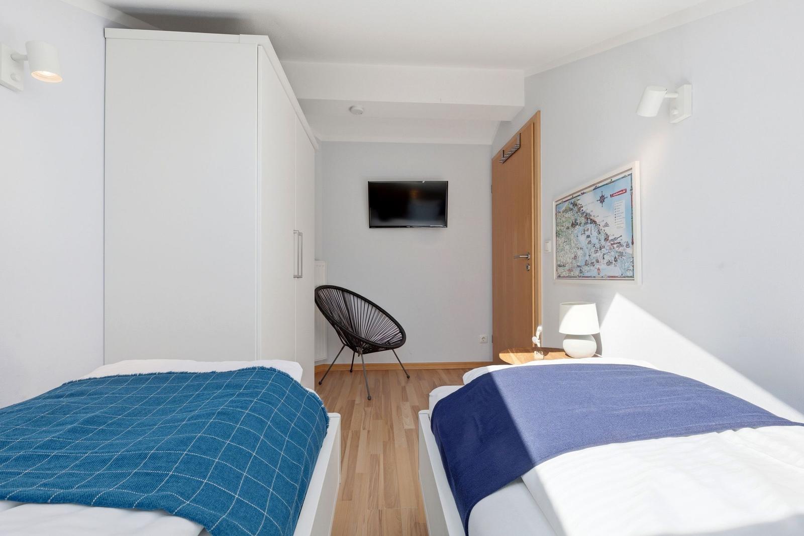 Zwei Betten mit blauen Decken, ein Fernseher und eine Tür im Schlafzimmer.
