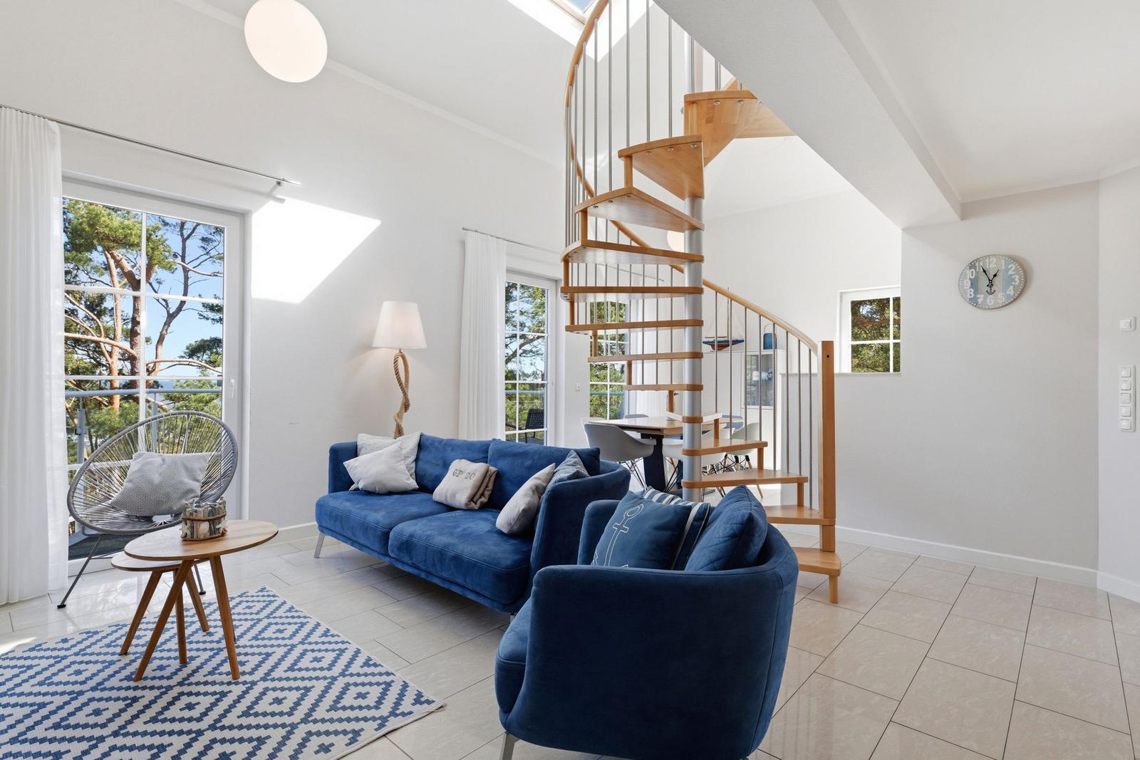 Wohnraum mit blauer Couch, Treppe und Fenster zur Aussicht.
