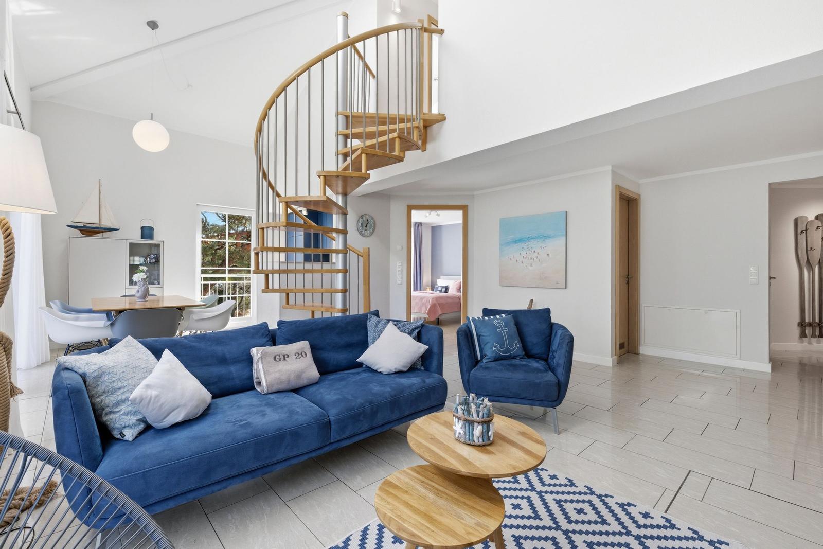 Wohnbereich mit blauem Sofa, Spiraltreppe und Blick in Schlafzimmer.