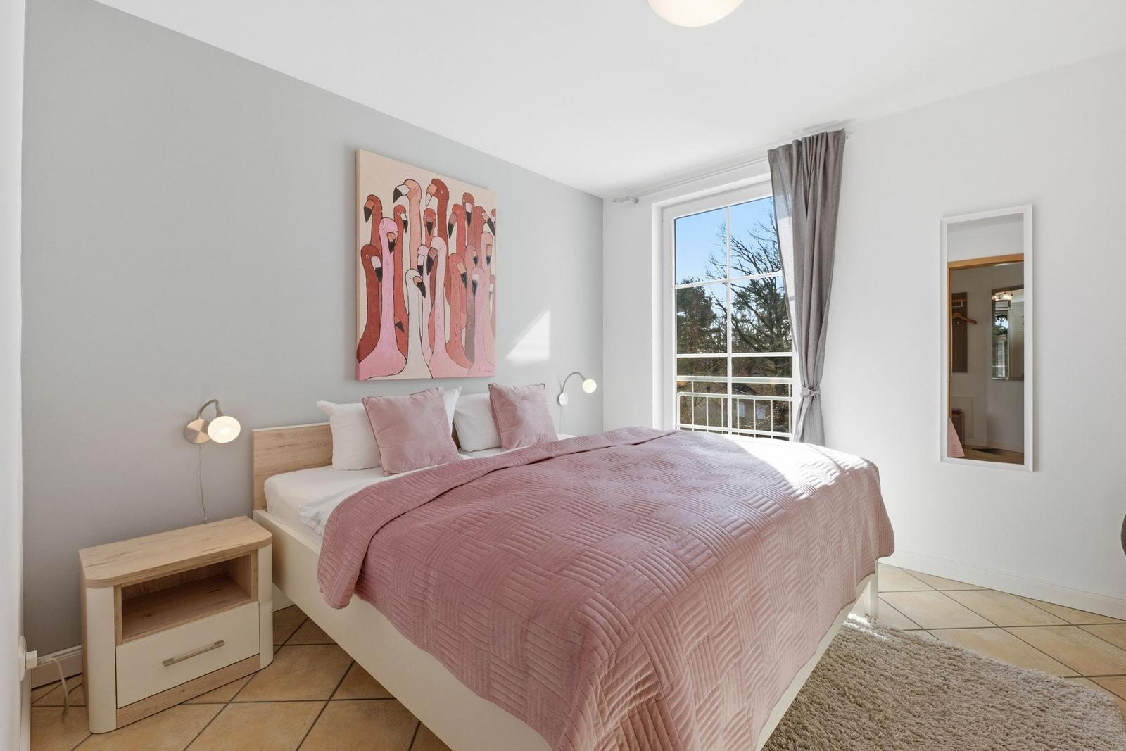 Schlafzimmer mit Bett, Wandbild und Fenster mit Blick auf Balkon.