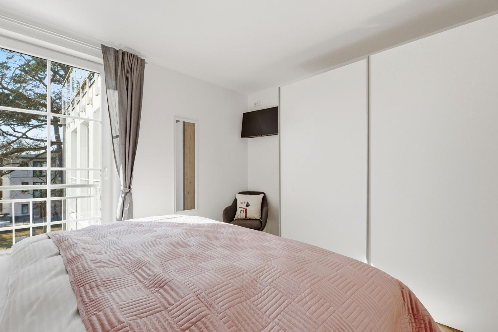 Schlafzimmer mit Bett, Fenster, Kleiderschrank und Sessel.