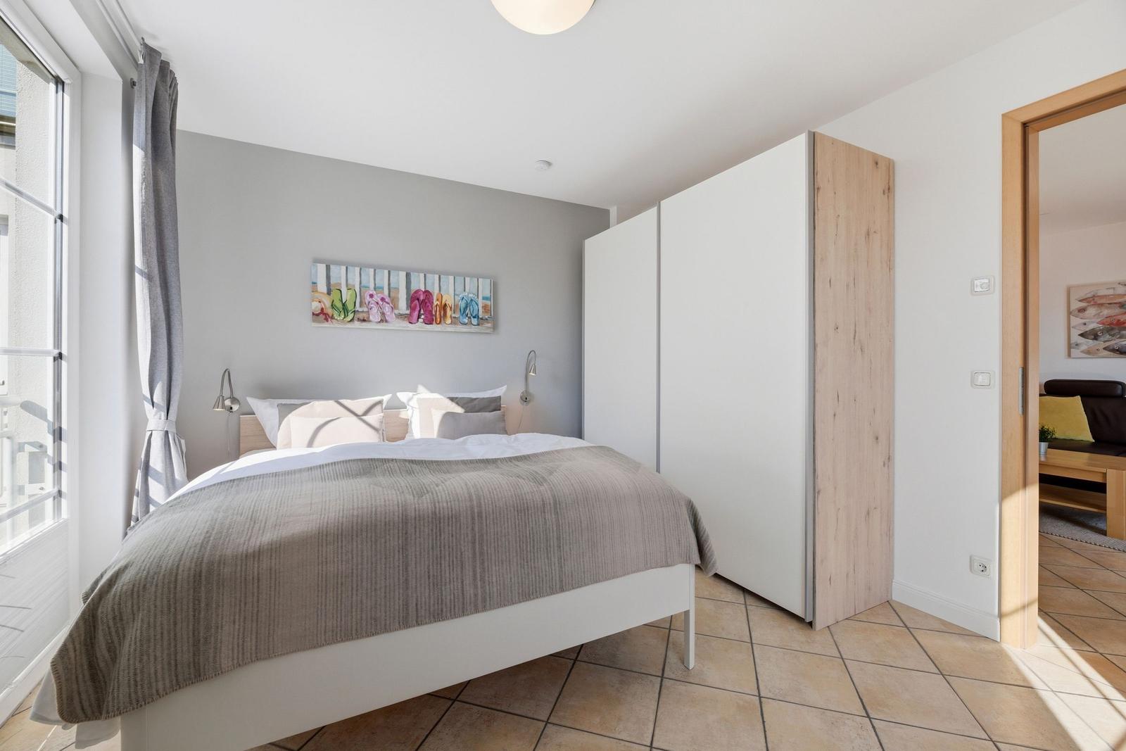 Schlafzimmer mit Bett, Schrank und Fenster. Wandbild mit bunten Flipflops.