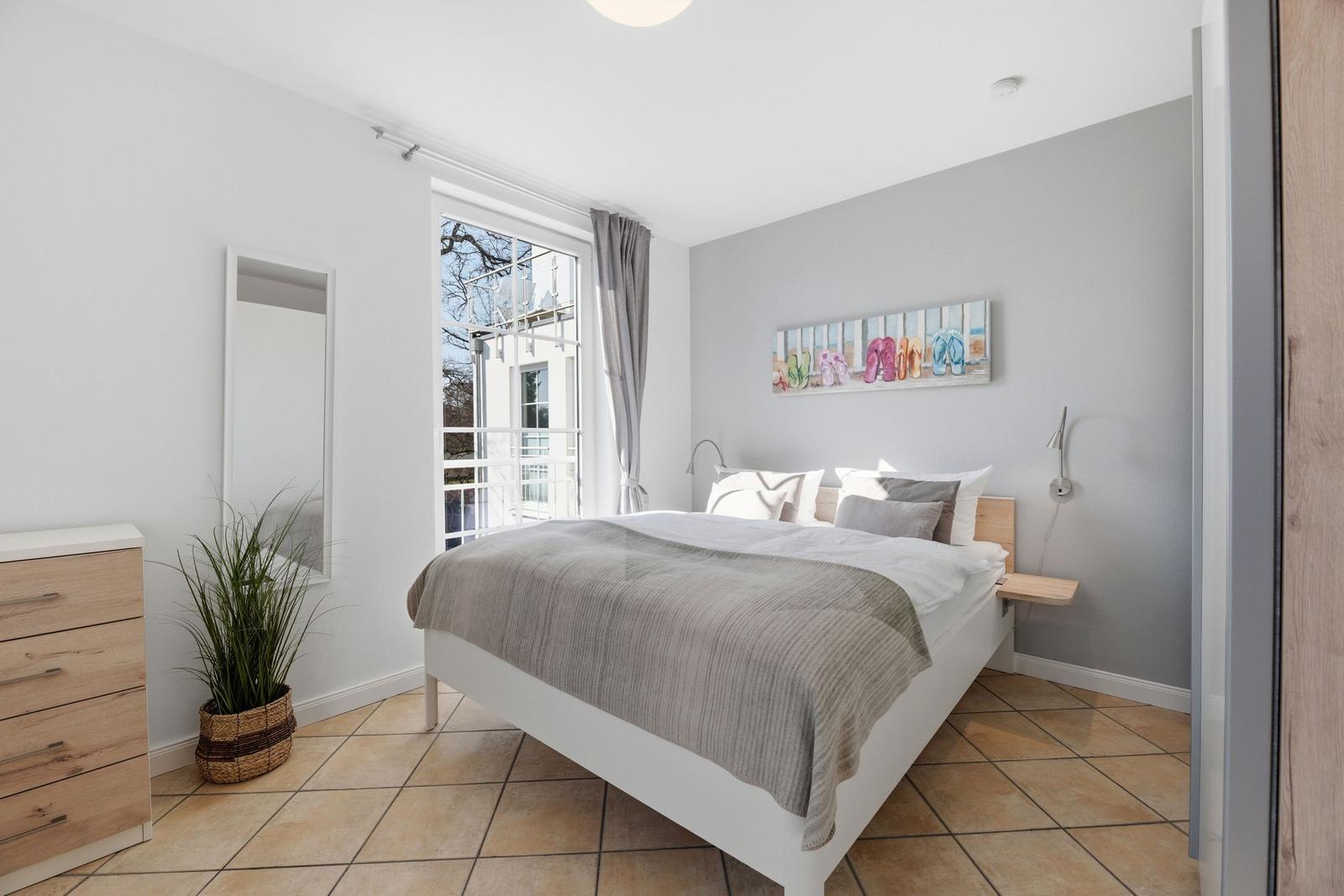 Schlafzimmer mit Bett, Fenster und Wandbild. Holzmöbel und Pflanze.
