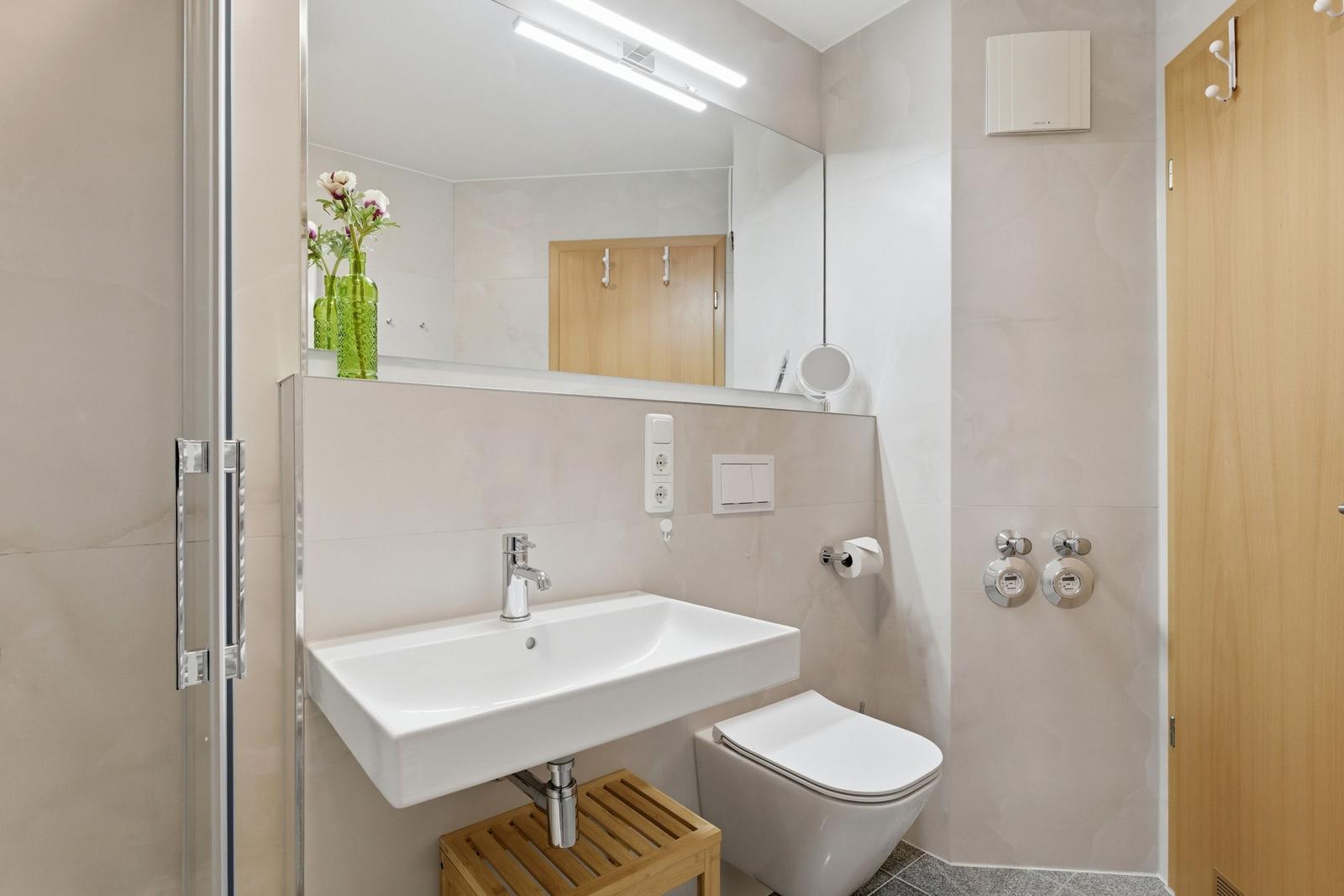 Badezimmer mit Waschbecken, Toilette und Spiegel. Holzstuhl unter dem Waschbecken.