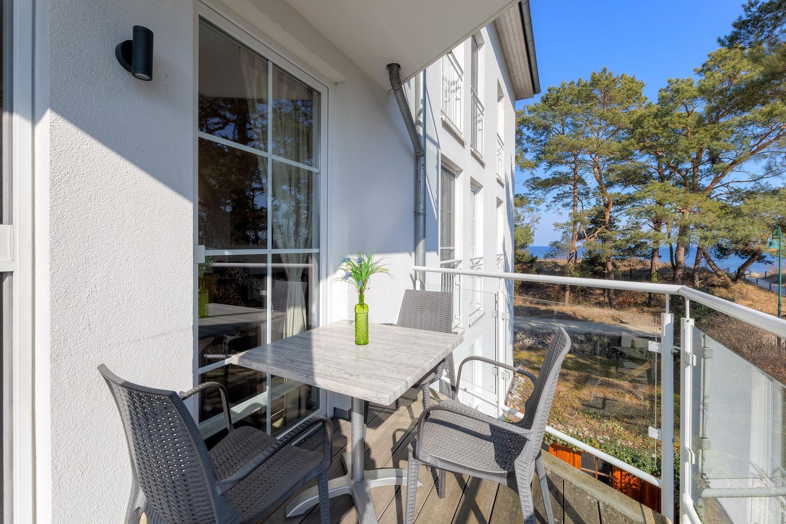 Terrasse mit Tisch und Stühlen, Blick auf Bäume und Meer.