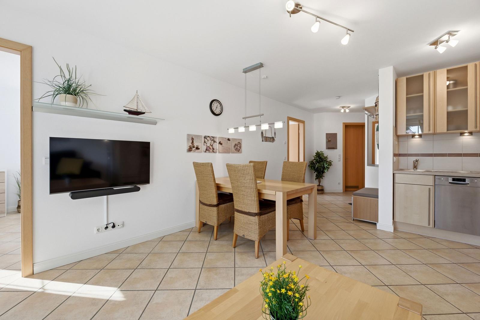 Wohn- und Essbereich mit Küchenzeile, Esstisch und Fernseher an der Wand.