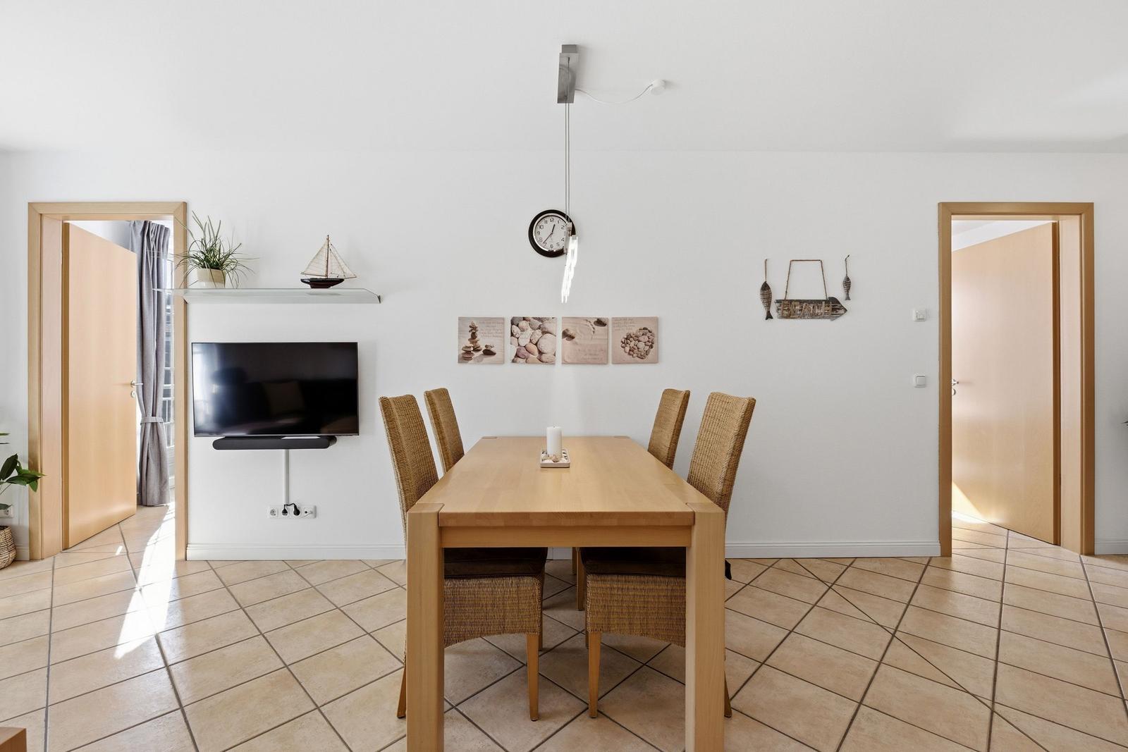Essbereich mit Holztisch, vier Stühlen und Fernseher an der Wand.
