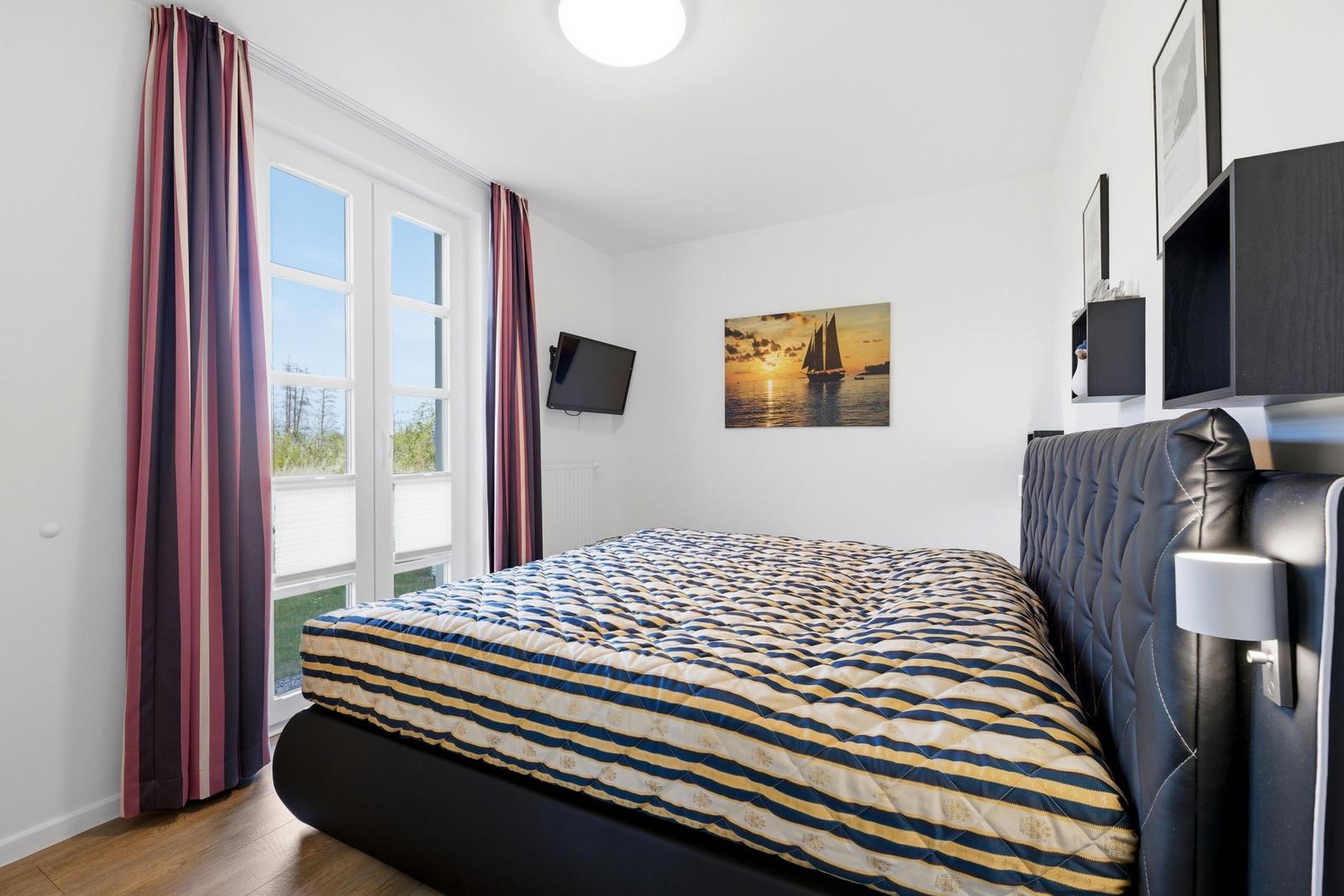 Schlafzimmer mit Bett, Fenster, Wandbild und TV.
