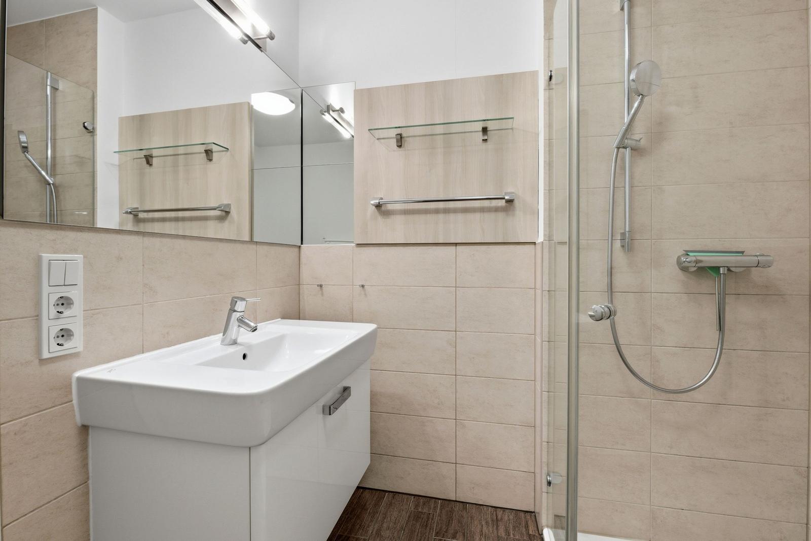 Badezimmer mit Dusche, Waschbecken und Spiegel.