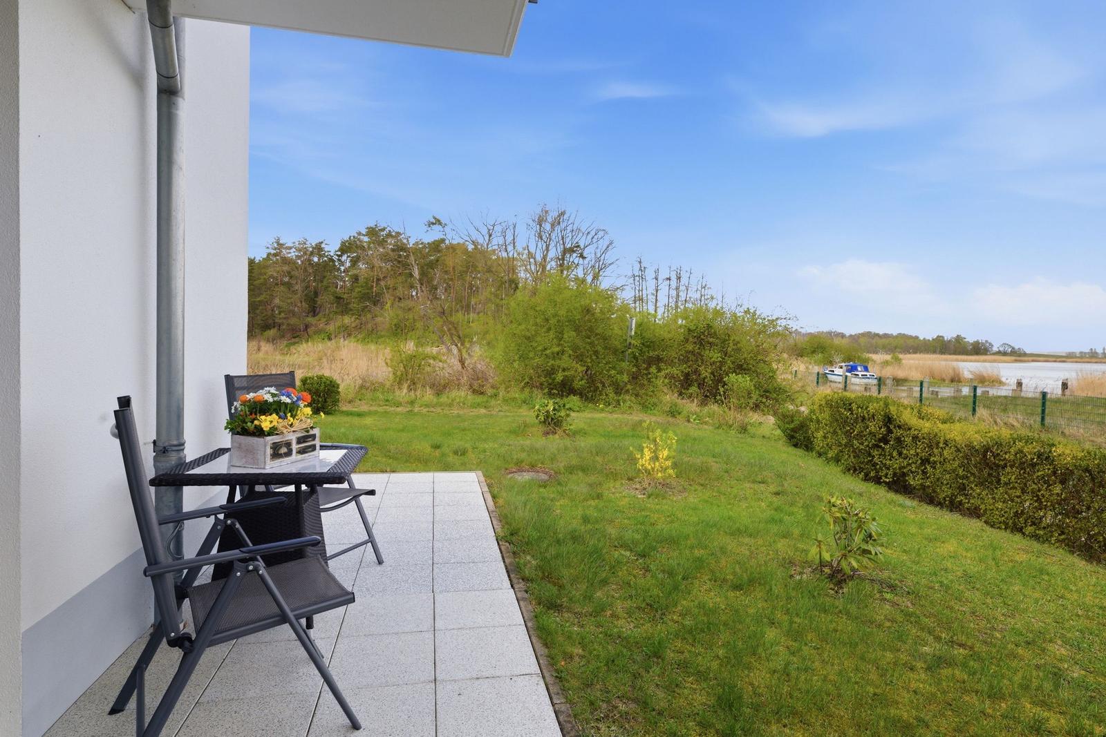 Terrasse mit Tisch und Stühlen, Blick auf Grünflächen und Wasser.