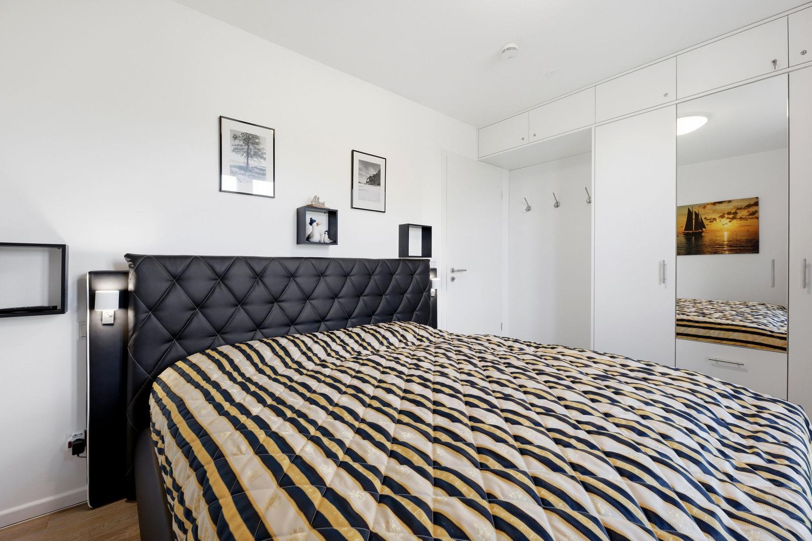 Schlafzimmer mit Bett, Kleiderschrank und Wandbildern.