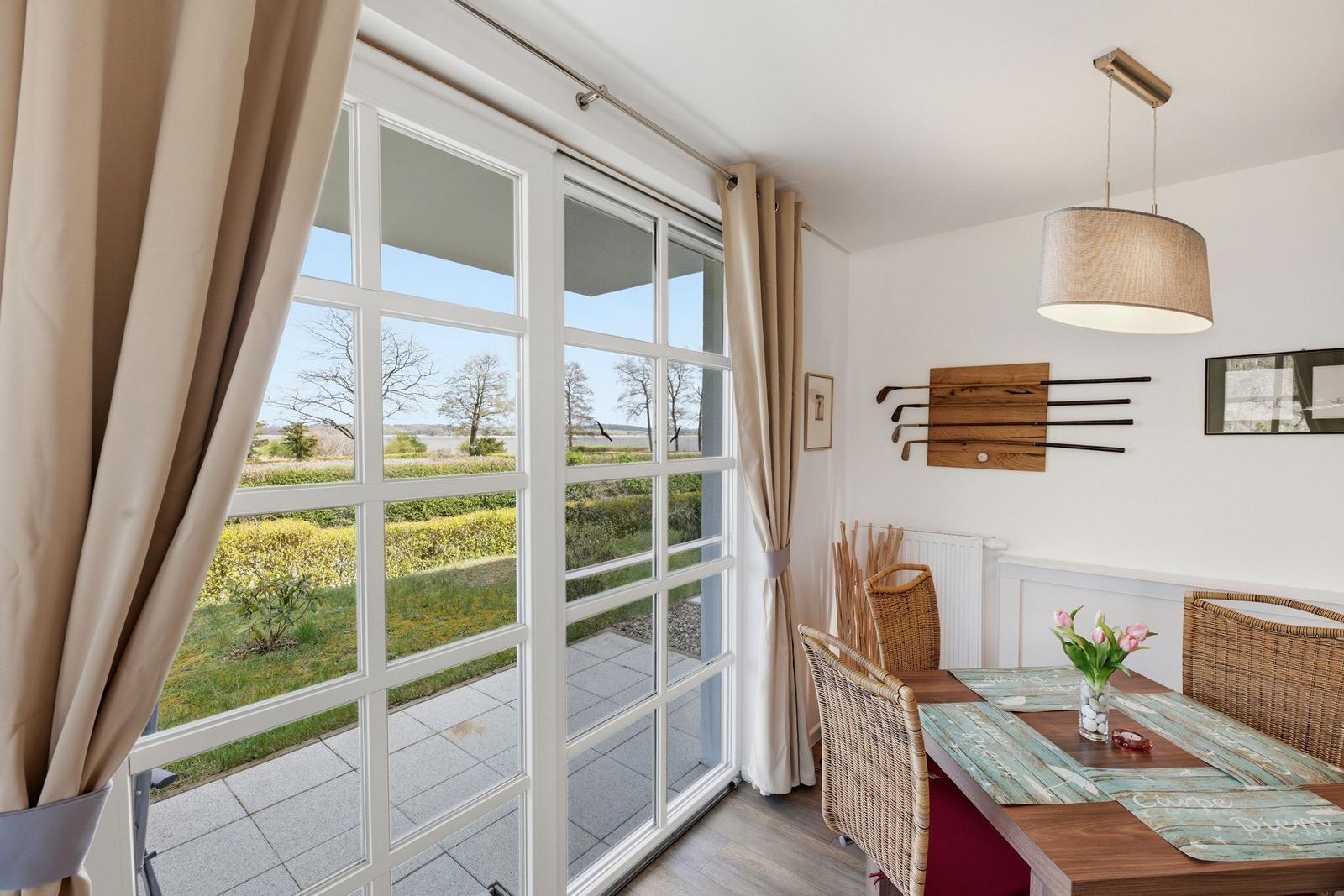 Esszimmer mit Tisch, Stühlen und Blick auf Garten. Golfschläger an Wand. Hängelampe und Blumen.