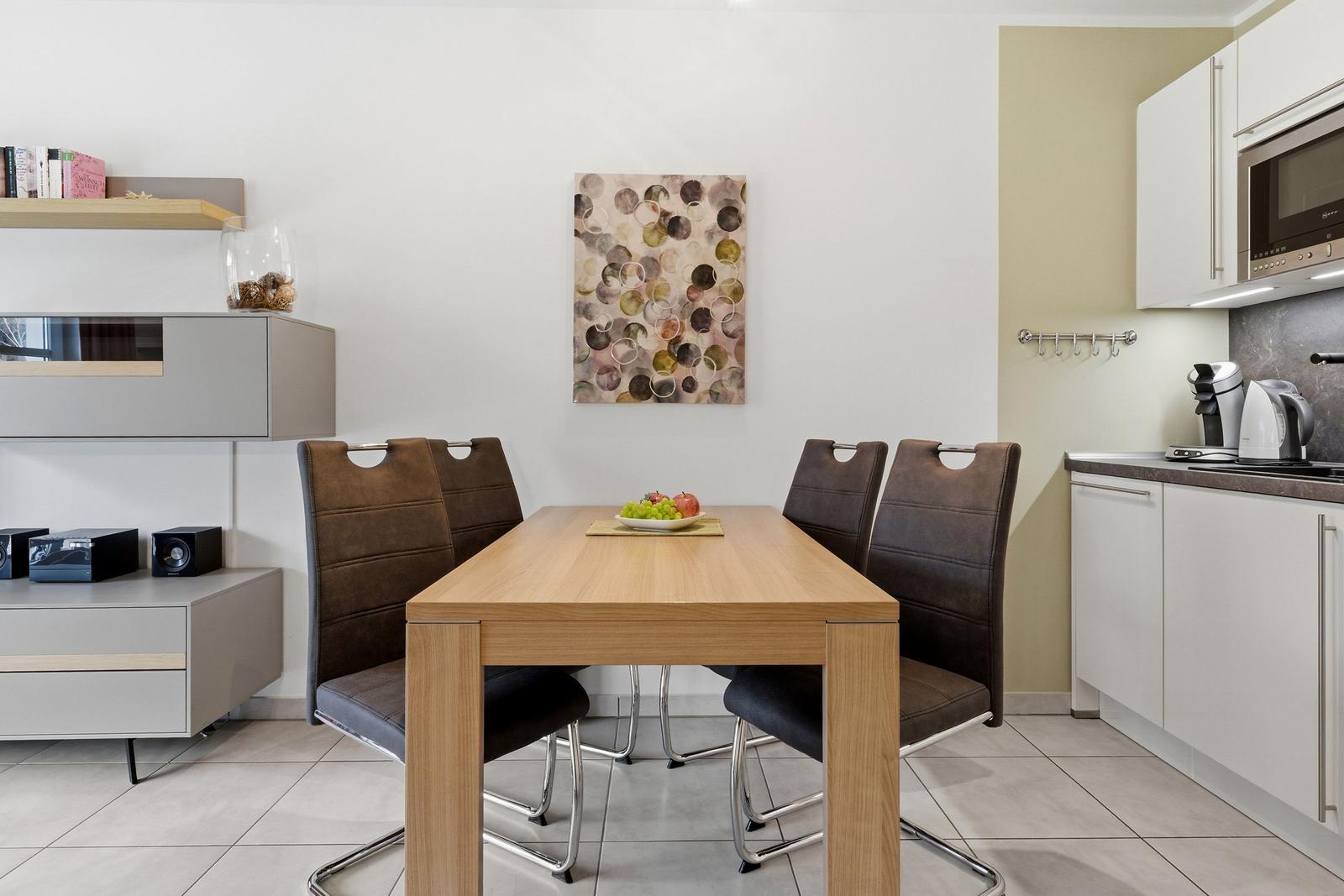 Esszimmer mit Holztisch, vier Stühlen und Küchenzeile im Hintergrund.