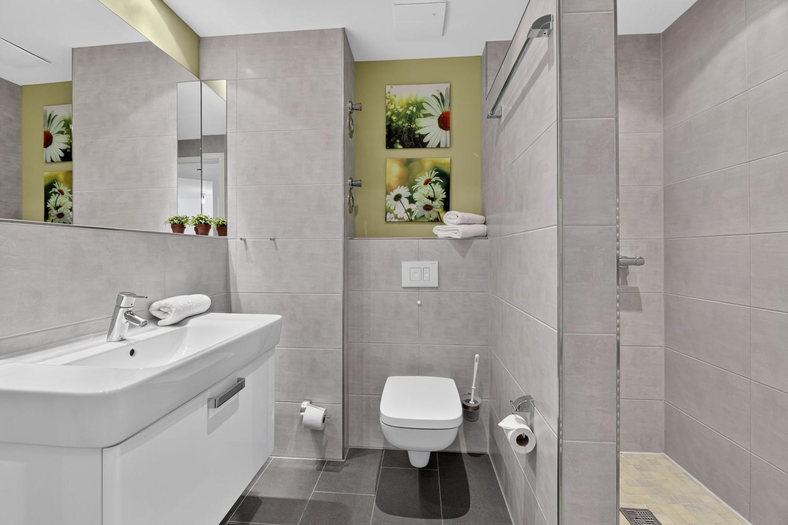 Badezimmer mit Dusche, Toilette und Waschbecken. Wandgestaltung mit Bildern von Blumen.