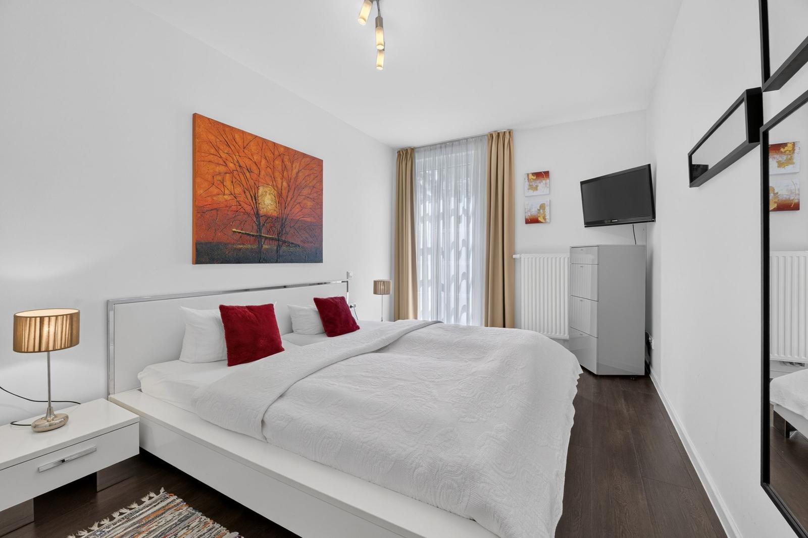 Schlafzimmer mit Doppelbett, Wandbild und Fernseher.
