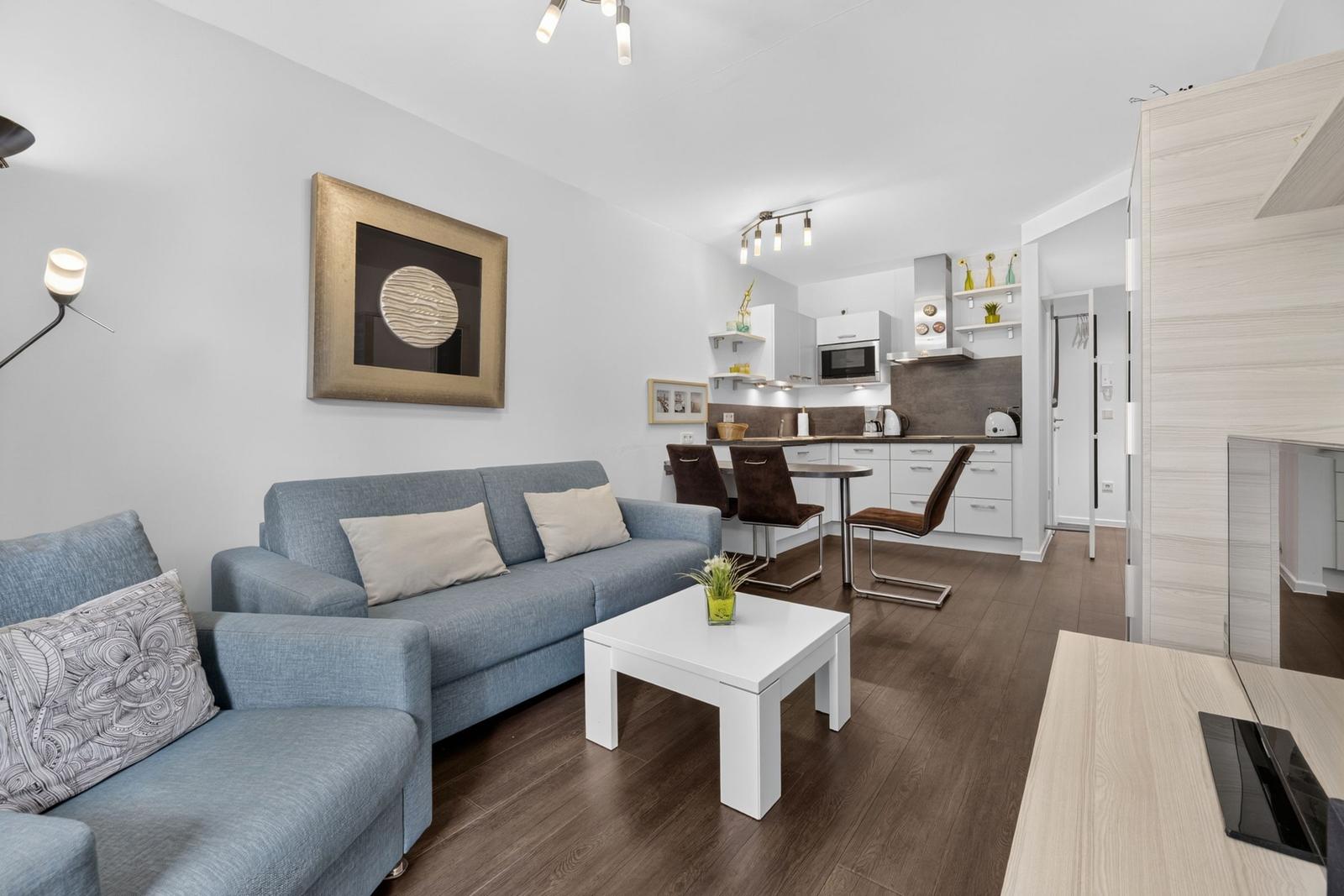 Wohnzimmer mit Sofa, Couchtisch und offener Küche im Hintergrund.