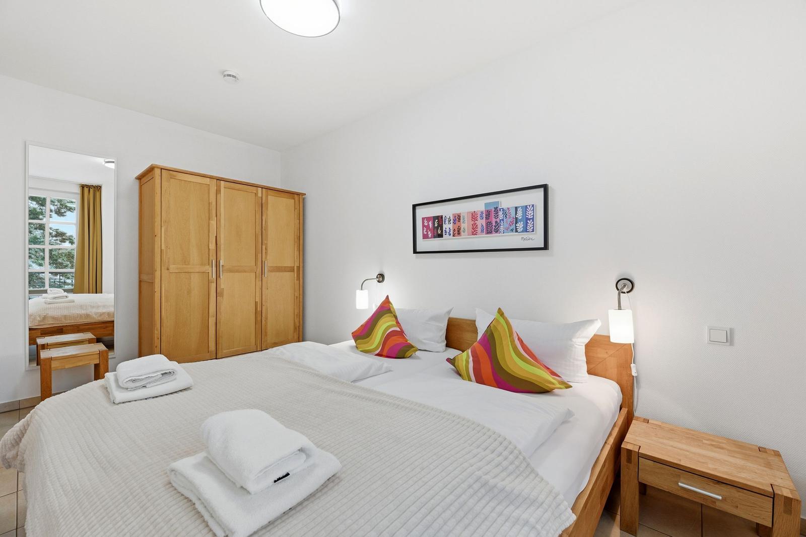 Schlafzimmer mit Doppelbett, Holzschrank und Nachttisch. Decke mit Kissen und Bild an der Wand.