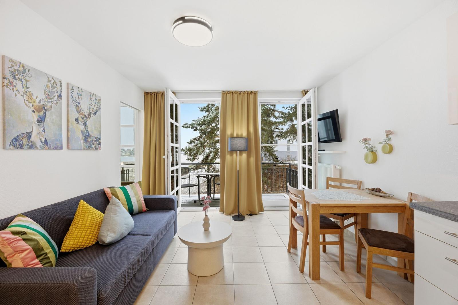 Wohn- und Essbereich mit Balkon, Sofa, Tisch und Wandbildern