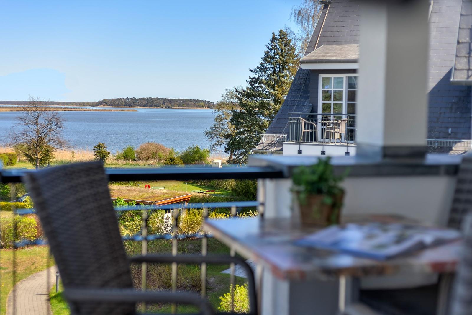 Balkon mit Sicht auf See und Garten. Tisch, Stühle und Pflanze sind sichtbar.