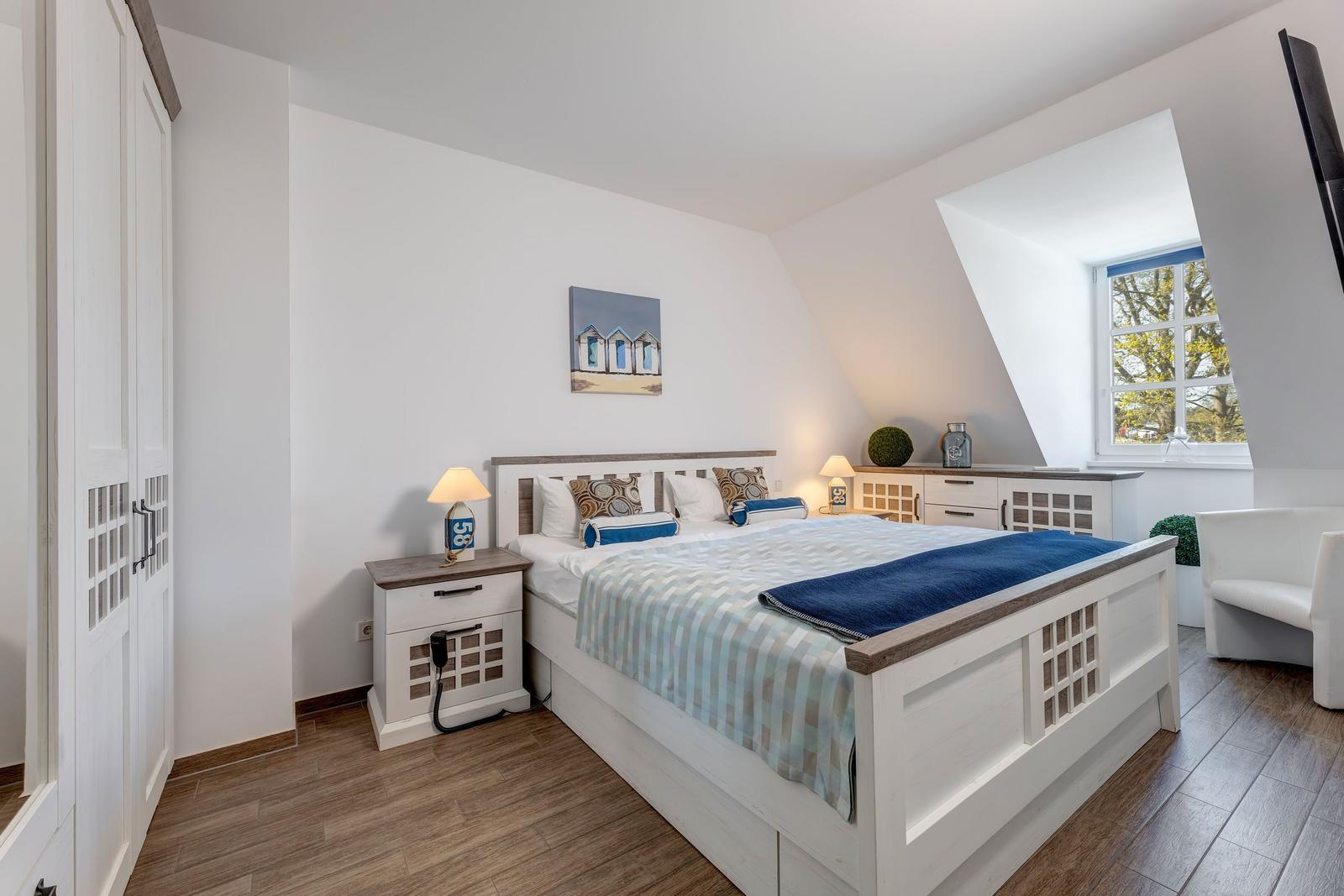 Schlafzimmer mit Dachschräge, Bett, Nachttisch, Fenster und Kleiderschrank.