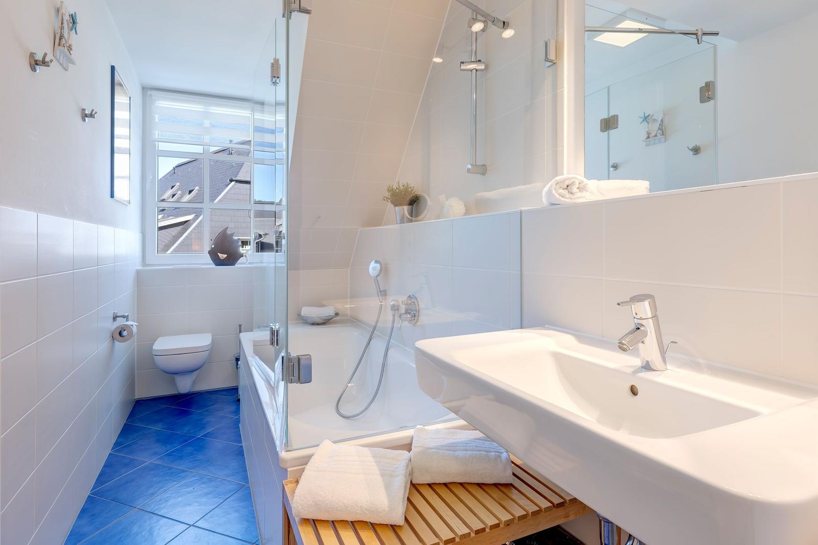 Badezimmer mit Dusche, Waschbecken und Toilette. Blaue Bodenfliesen und Spiegel.