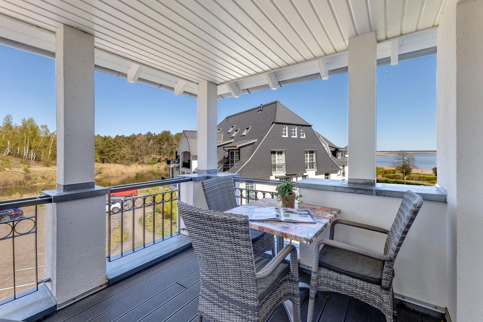 Terrasse mit Tisch und Stühlen, Blick auf Haus und Wasser.