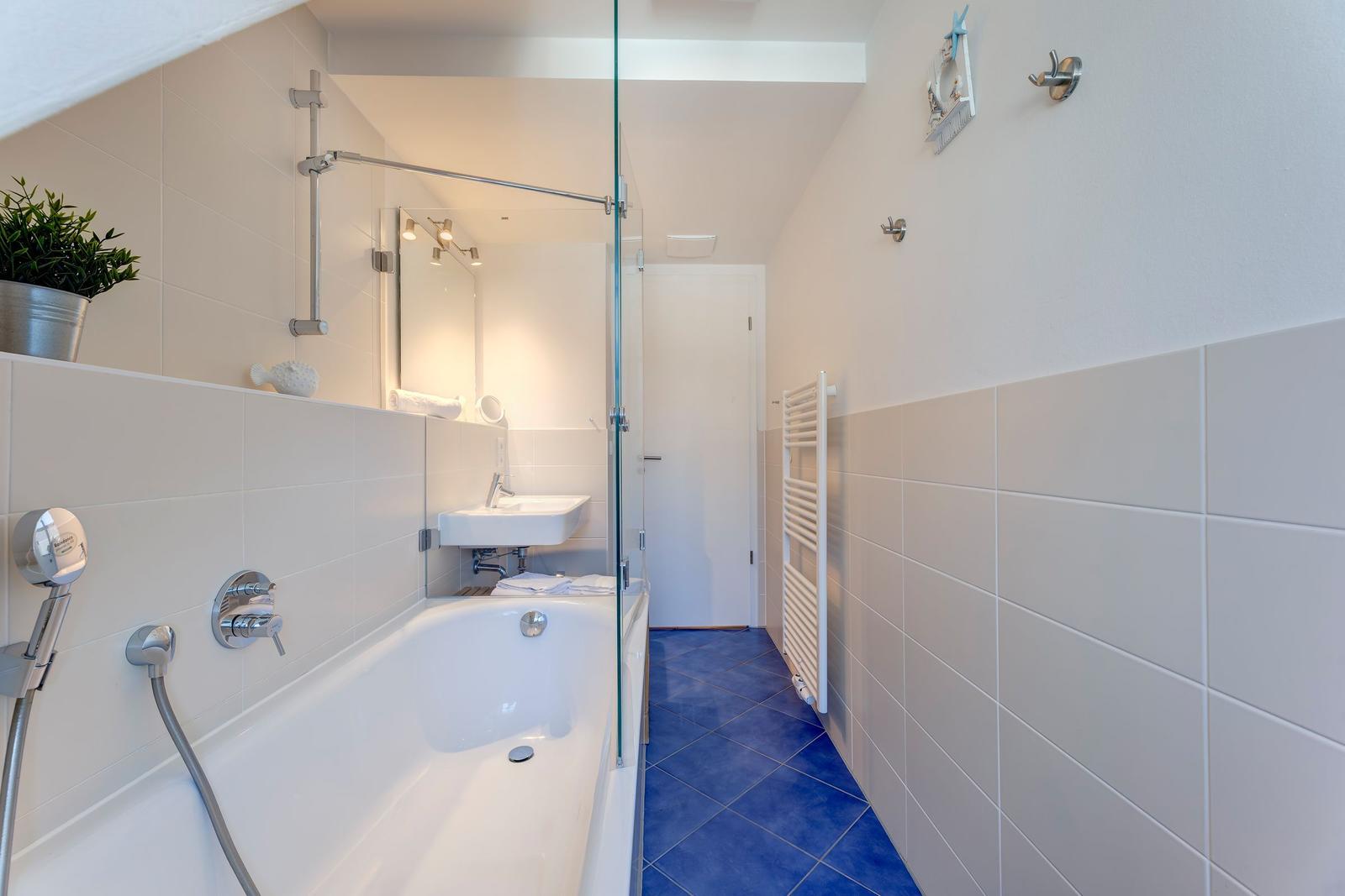 Badezimmer mit Badewanne, Dusche, Waschbecken und Heizkörper.