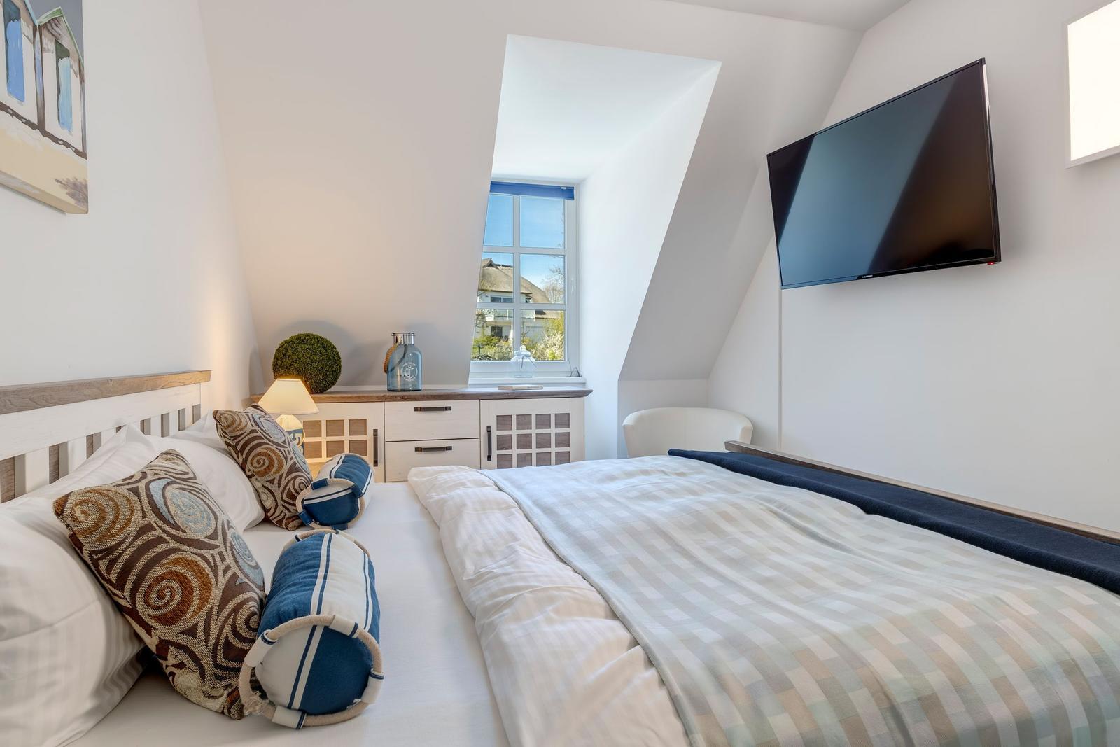 Schlafzimmer mit Dachfenster, Bett, Fernseher und Schrank.
