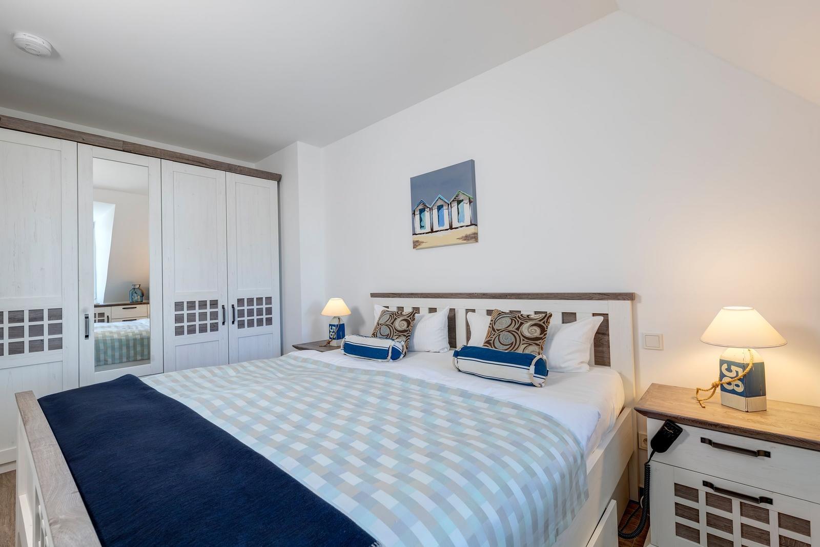 Schlafzimmer mit Bett, Nachttischen und Kleiderschrank. Wandbild mit Strandhütten.