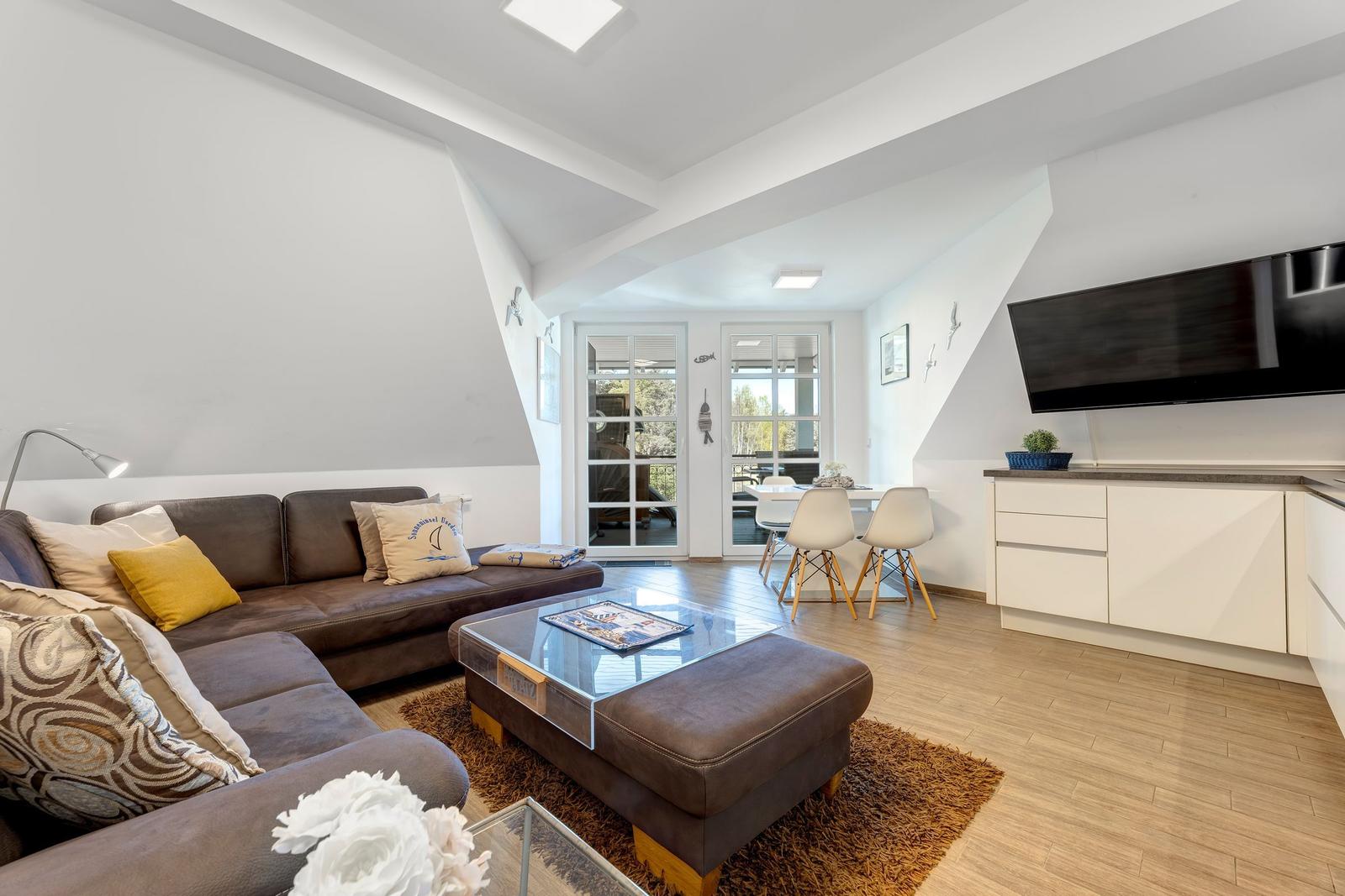 Wohnbereich mit Sofa, Couchtisch und TV. Essbereich mit Tisch und Stühlen. Holzboden und Fenster.