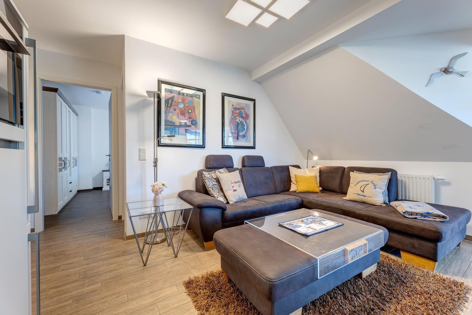 Wohnzimmer mit Sofa, Couchtisch und Wandbildern unter Dachschräge.